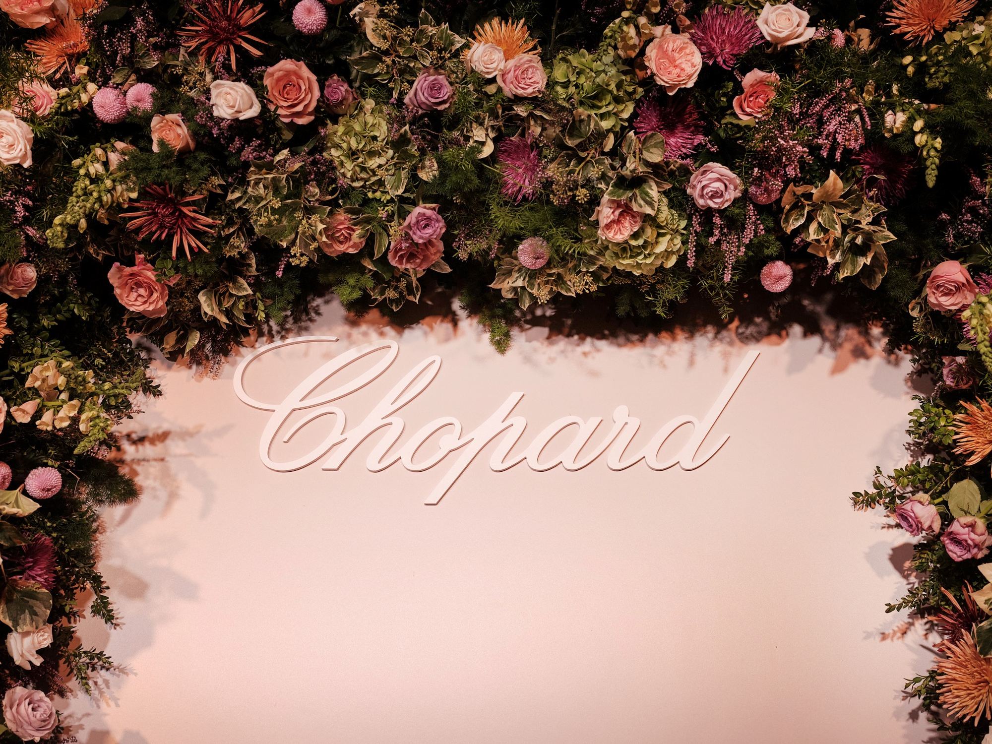 Arco de flores rosas y silvestres alrededor del logotipo de Chopard sobre un panel rosa, escenografía del evento Chopard producido por ESMA Events