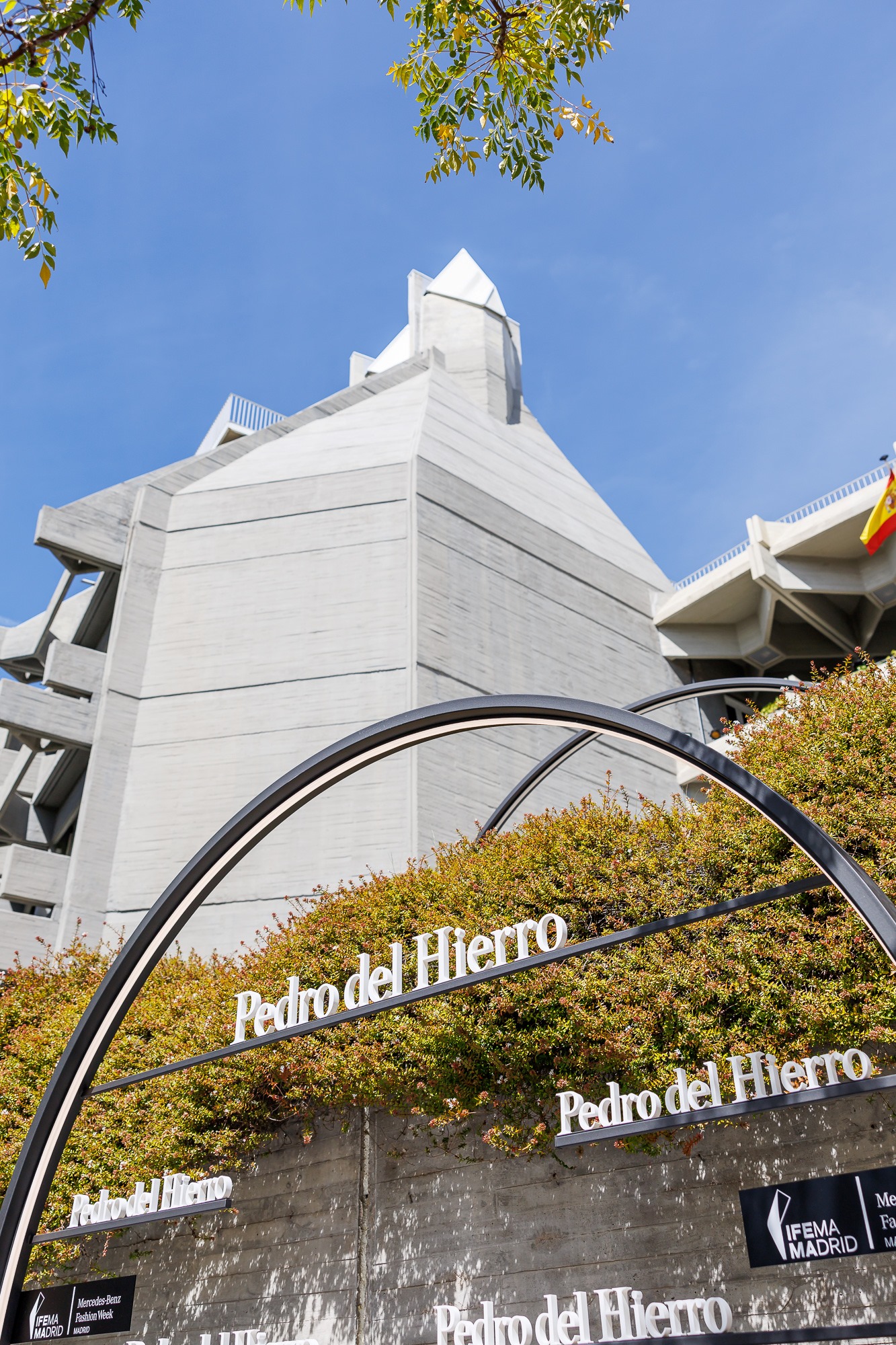 Arco metálico con el nombre Pedro del Hierro frente al edificio y vegetación, desfile Pedro del Hierro SS25 producido por ESMA Events