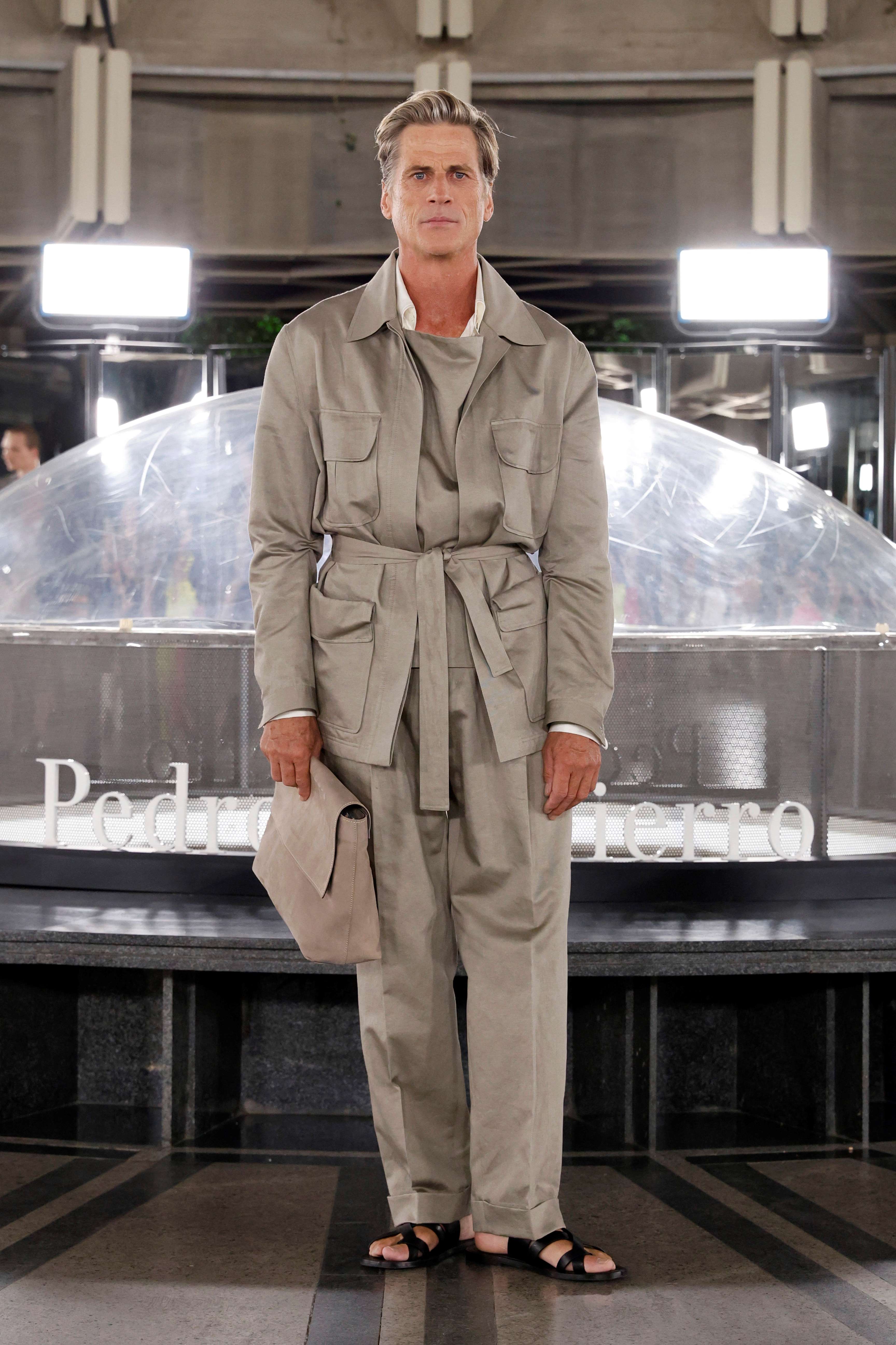 Modelo masculino con traje safari beis y sombrero en la mano ante la cúpula con el nombre Pedro del Hierro, desfile Pedro del Hierro SS25 producido por ESMA Events