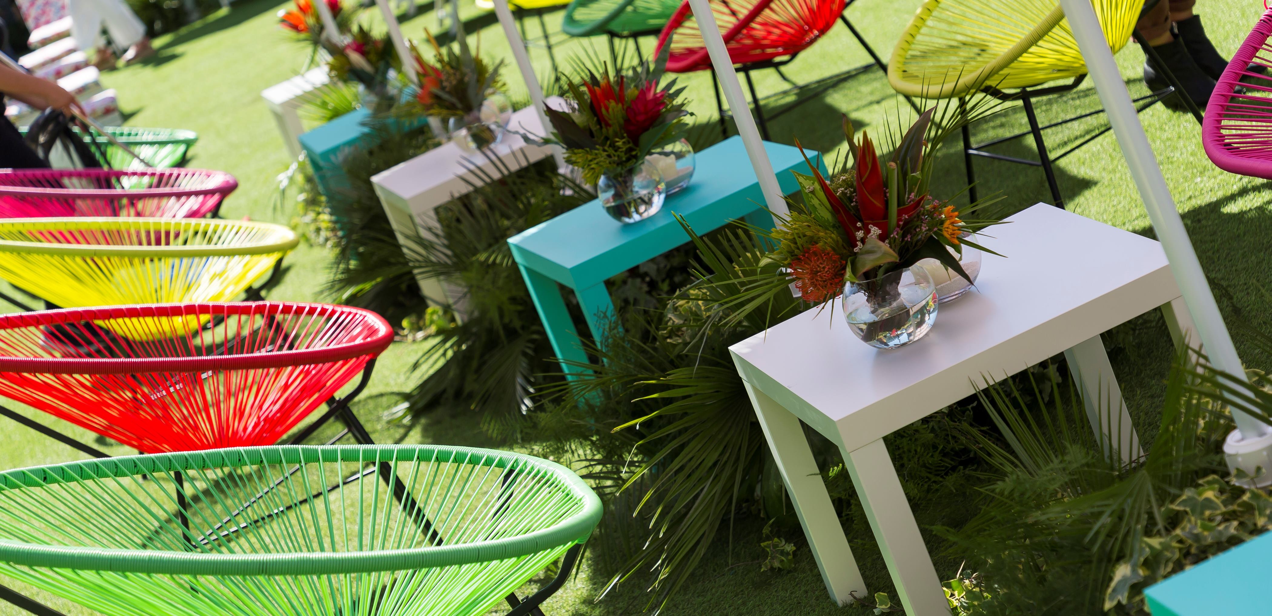 Sillas de colores fluorescentes y mesas blancas con flores tropicales sobre el césped, evento Women'secret Nos gusta el verano producido por ESMA Events