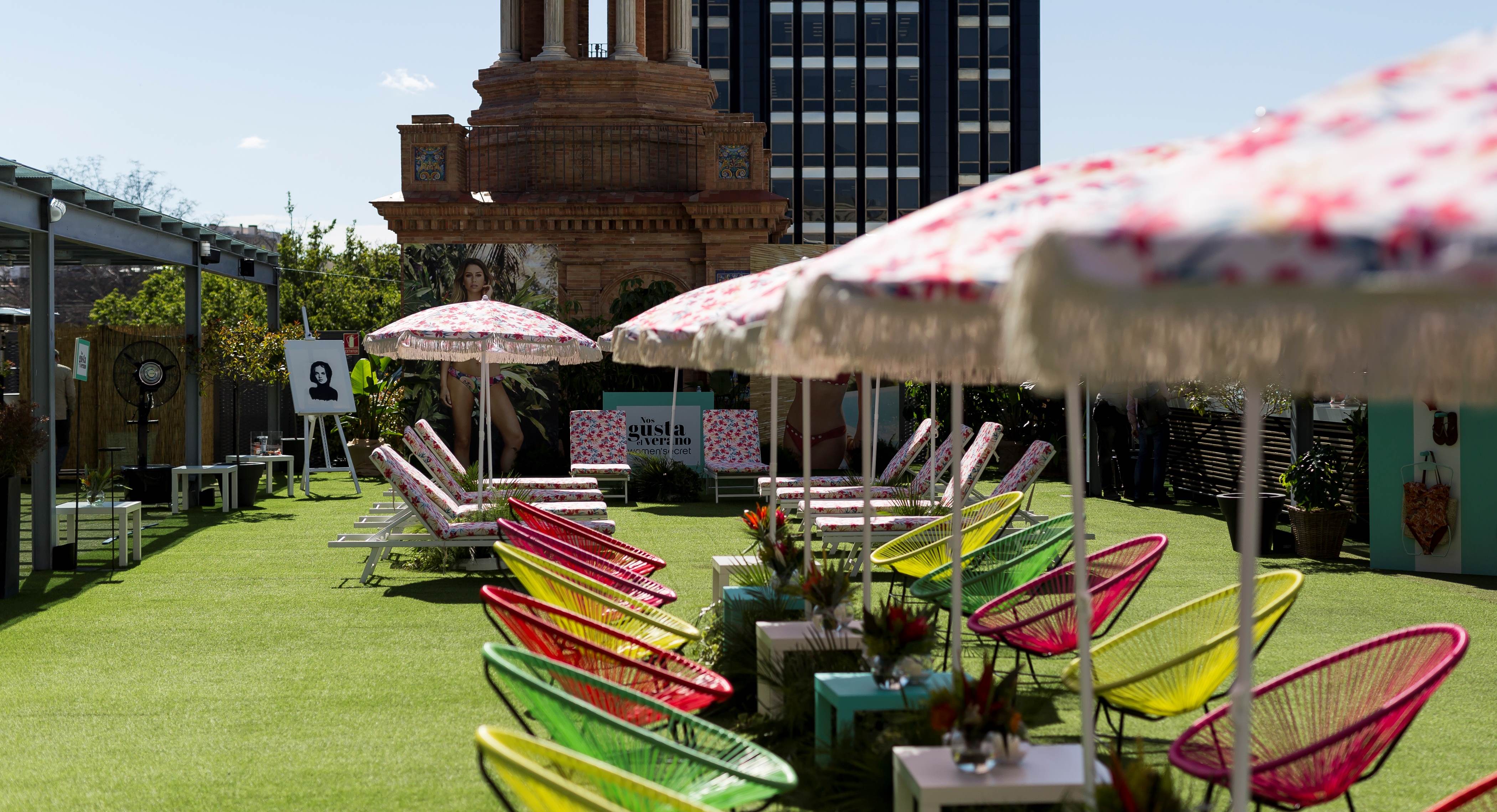 Zona de descanso con sillas de colores, sombrillas de flores y la torre histórica al fondo, evento Women'secret Nos gusta el verano producido por ESMA Events