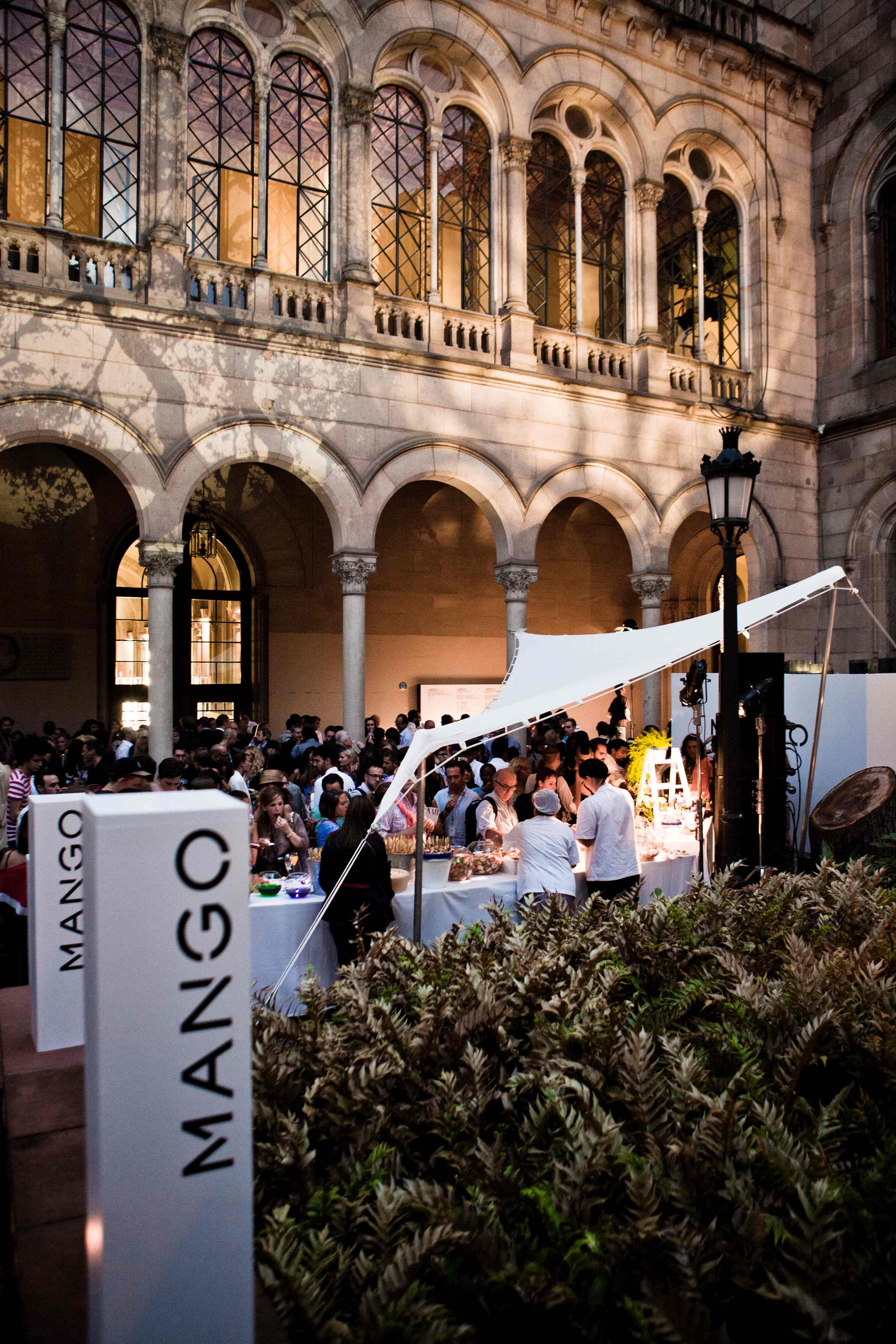 Patio con arcos y tótem blanco de Mango junto a una carpa blanca llena de invitados, cocktail party de Mango producida por ESMA Events