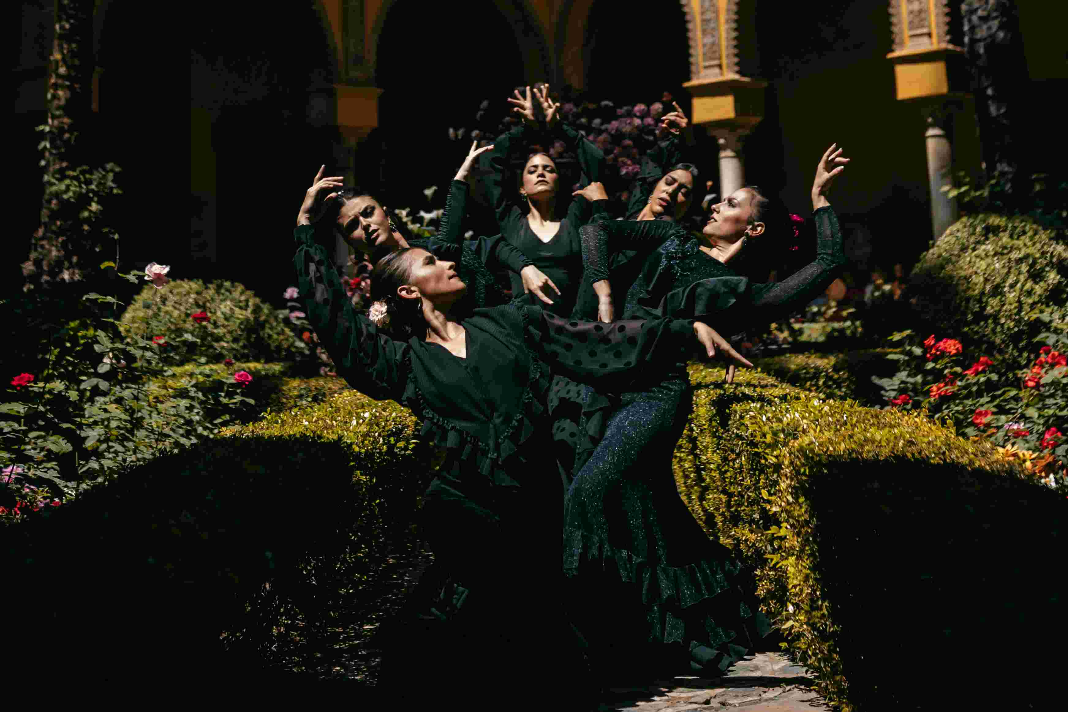 Grupo de bailarinas con vestidos verdes oscuros en pose entre setos y flores, desfile IQ Collection producido por ESMA Events