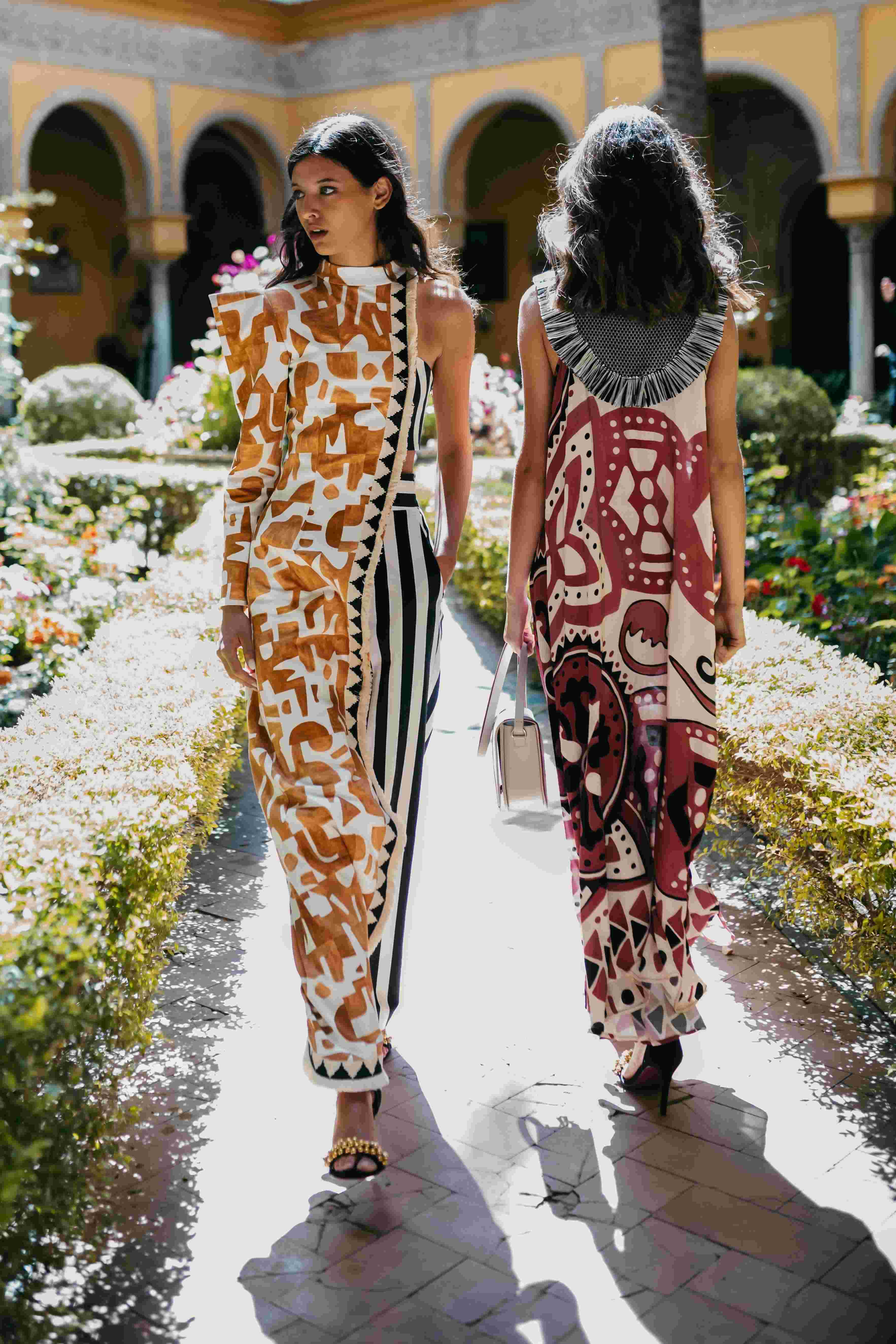 Dos modelos con conjuntos estampados caminando por un sendero entre setos, desfile IQ Collection producido por ESMA Events