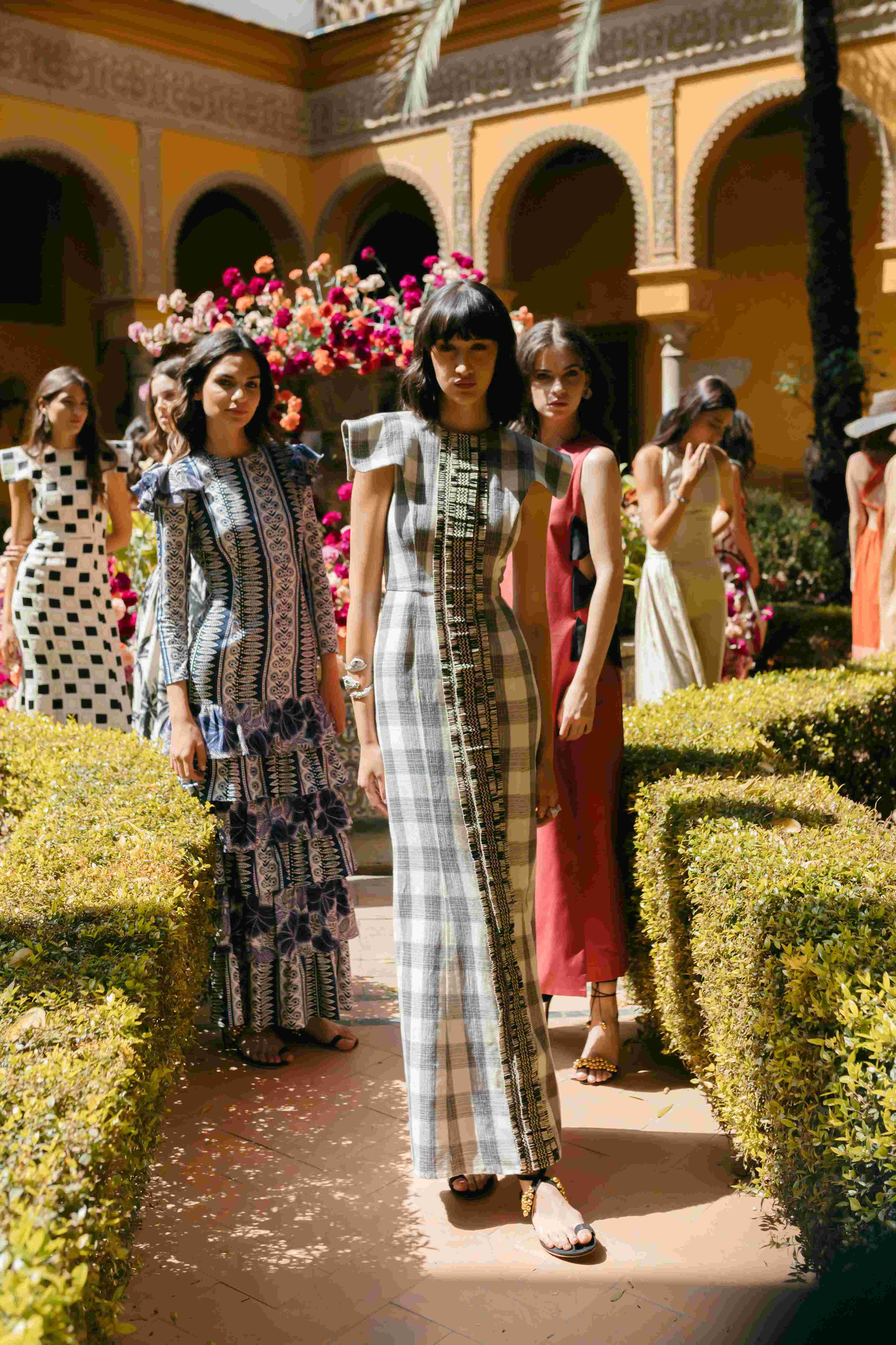 Modelos con vestidos de cuadros y volantes avanzando por el jardín del patio, desfile IQ Collection producido por ESMA Events