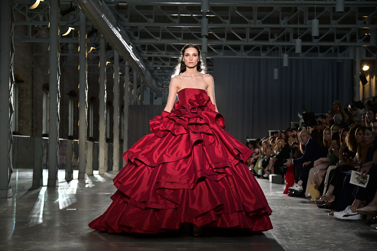 Model in a red dress with a large ruffled skirt in an industrial hall with an audience, Lola Flores Centenary exhibition by Redondo Brand produced by ESMA Events