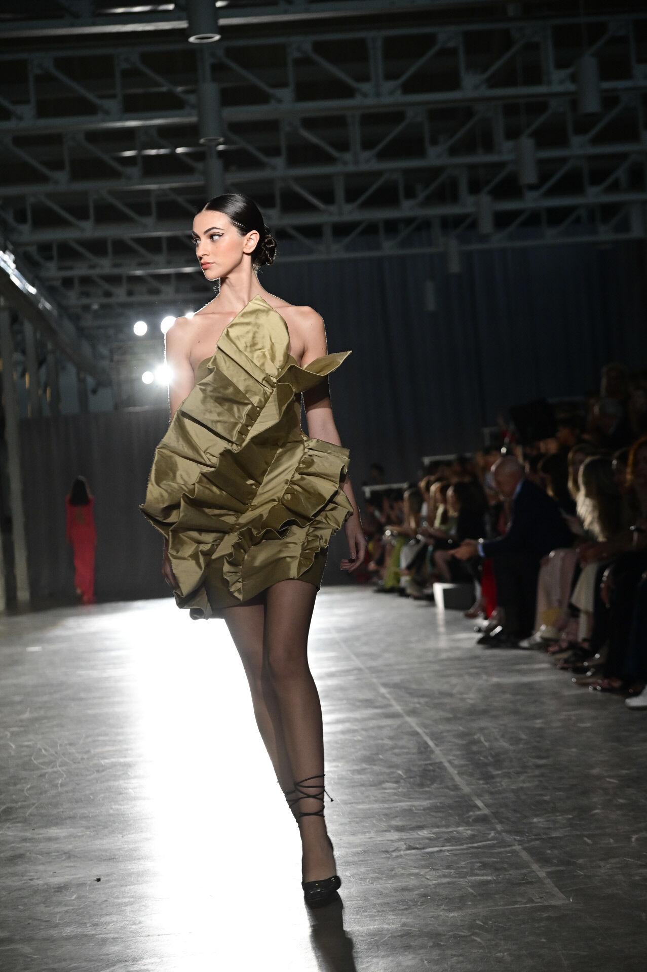 Model in a short gold dress with sculptural volume walking in front of the audience, Lola Flores Centenary exhibition by Redondo Brand produced by ESMA Events