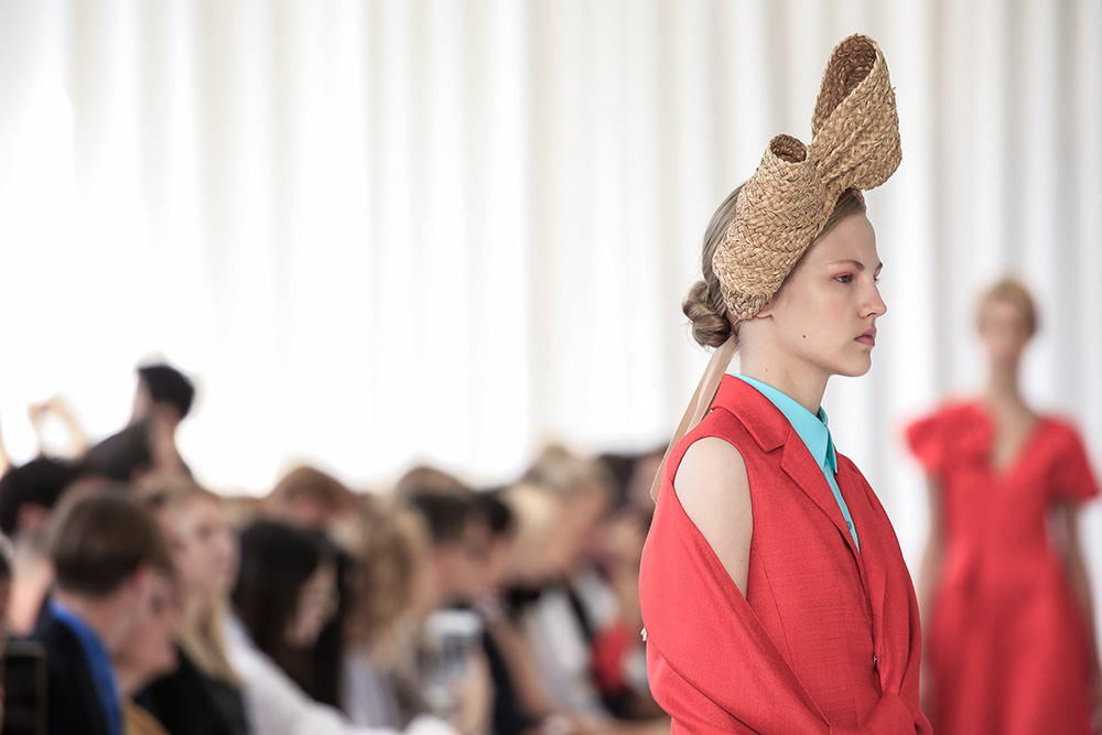 Perfil de una modelo con lazo de rafia y chaqueta coral ante el público desenfocado, desfile Delpozo Nueva York SS 2018 producido por ESMA Events