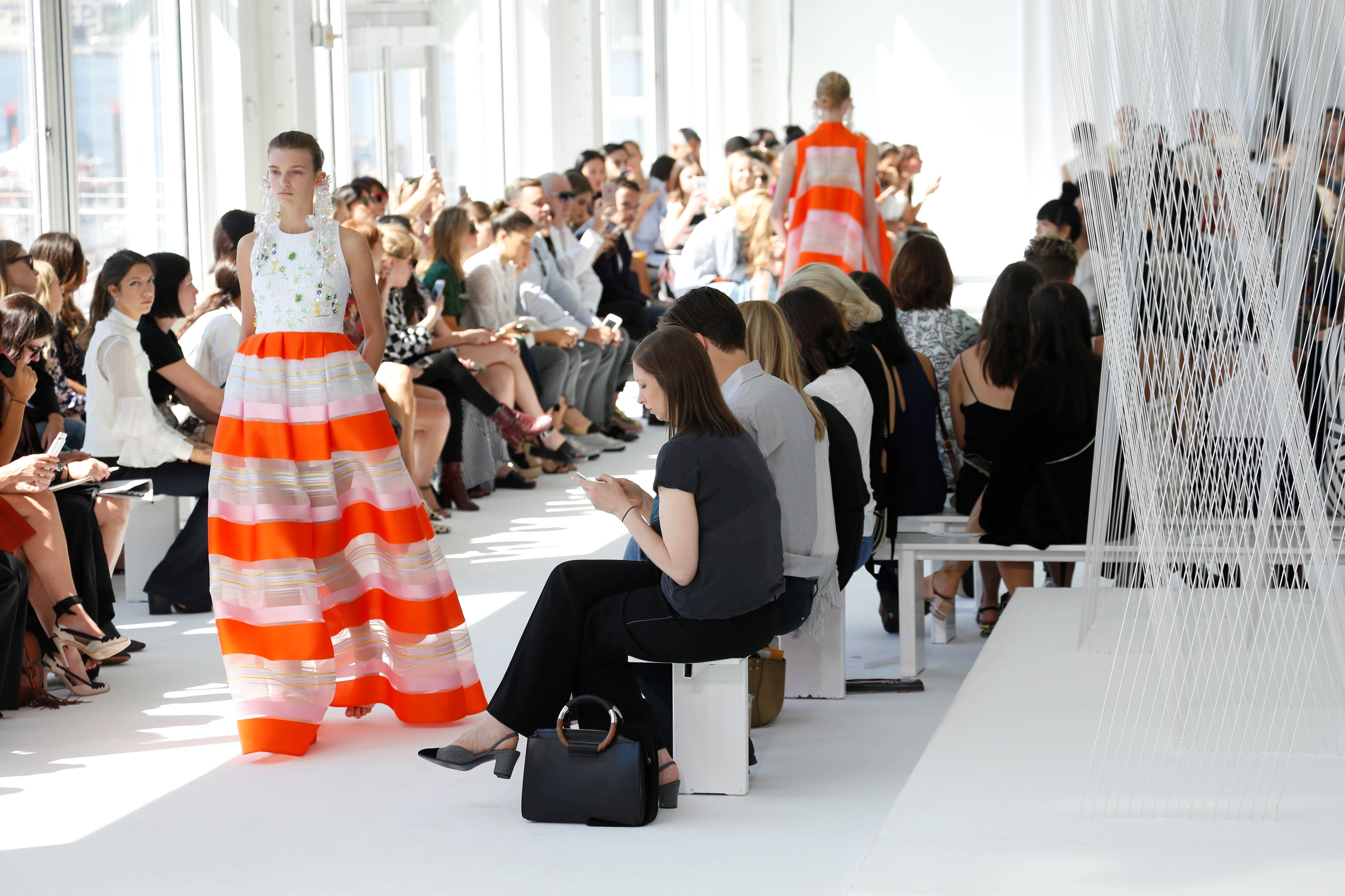 Modelo con falda de rayas naranjas y blancas caminando entre el público bajo cortinas de hilos blancos, desfile Delpozo Nueva York SS 2017 producido por ESMA Events
