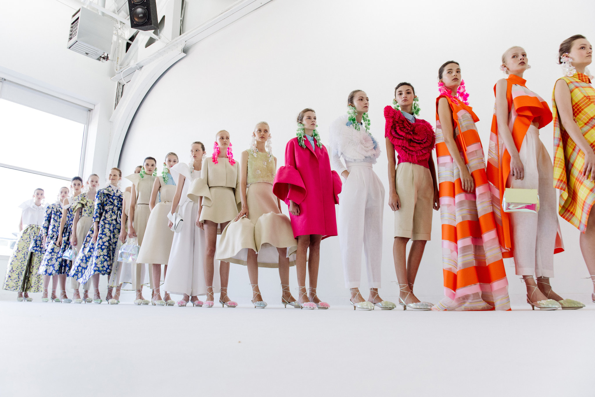 Fila de modelos con vestidos de flores, rayas naranjas y prendas fucsia posando en la sala blanca, desfile Delpozo Nueva York SS 2017 producido por ESMA Events