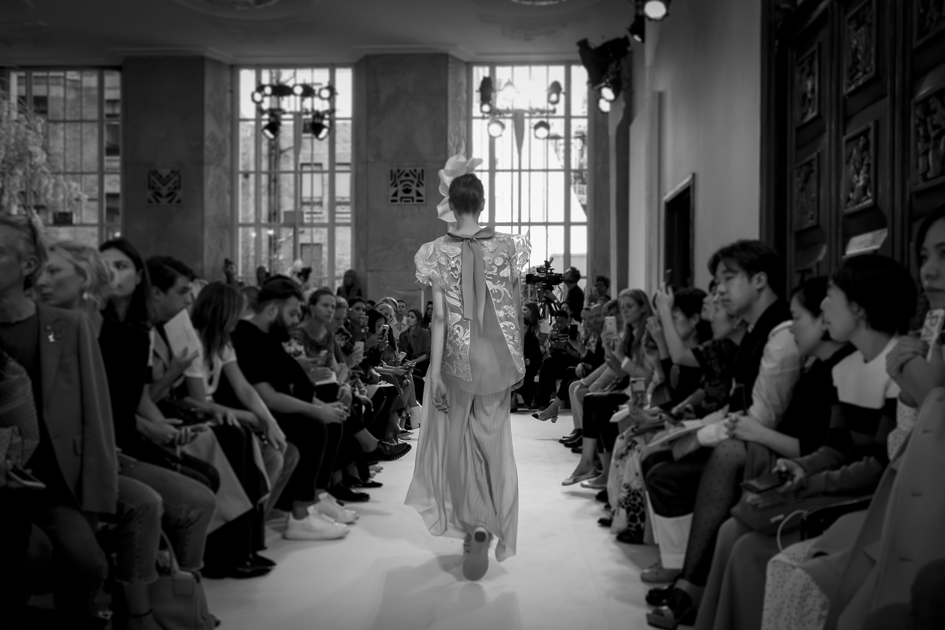 Modelo de espaldas con vestido plateado caminando entre el público, en blanco y negro, desfile Delpozo Londres SS 2019 producido por ESMA Events