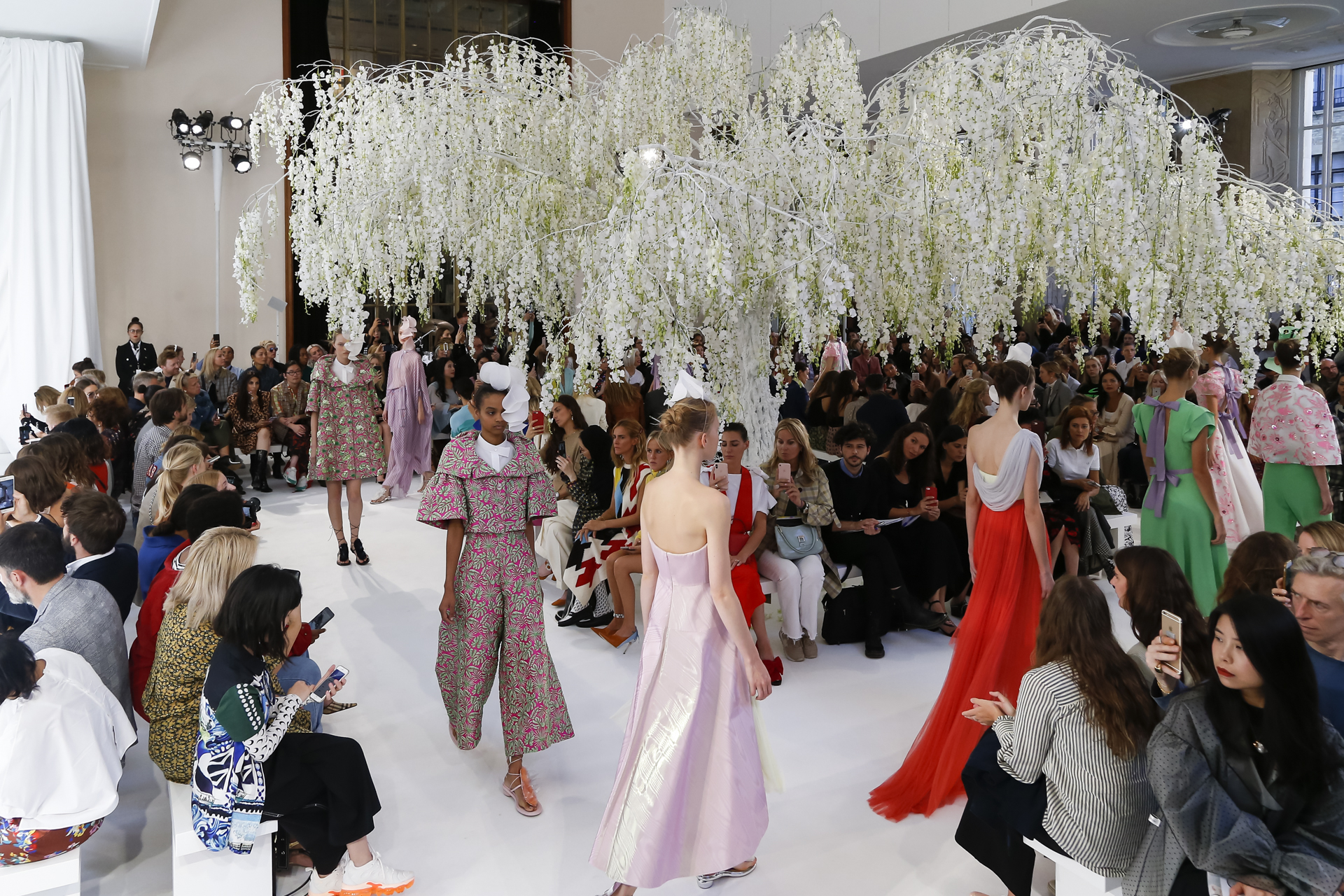 Modelos con vestidos de colores bajo un sauce de glicinias blancas durante el desfile, desfile Delpozo Londres SS 2019 producido por ESMA Events