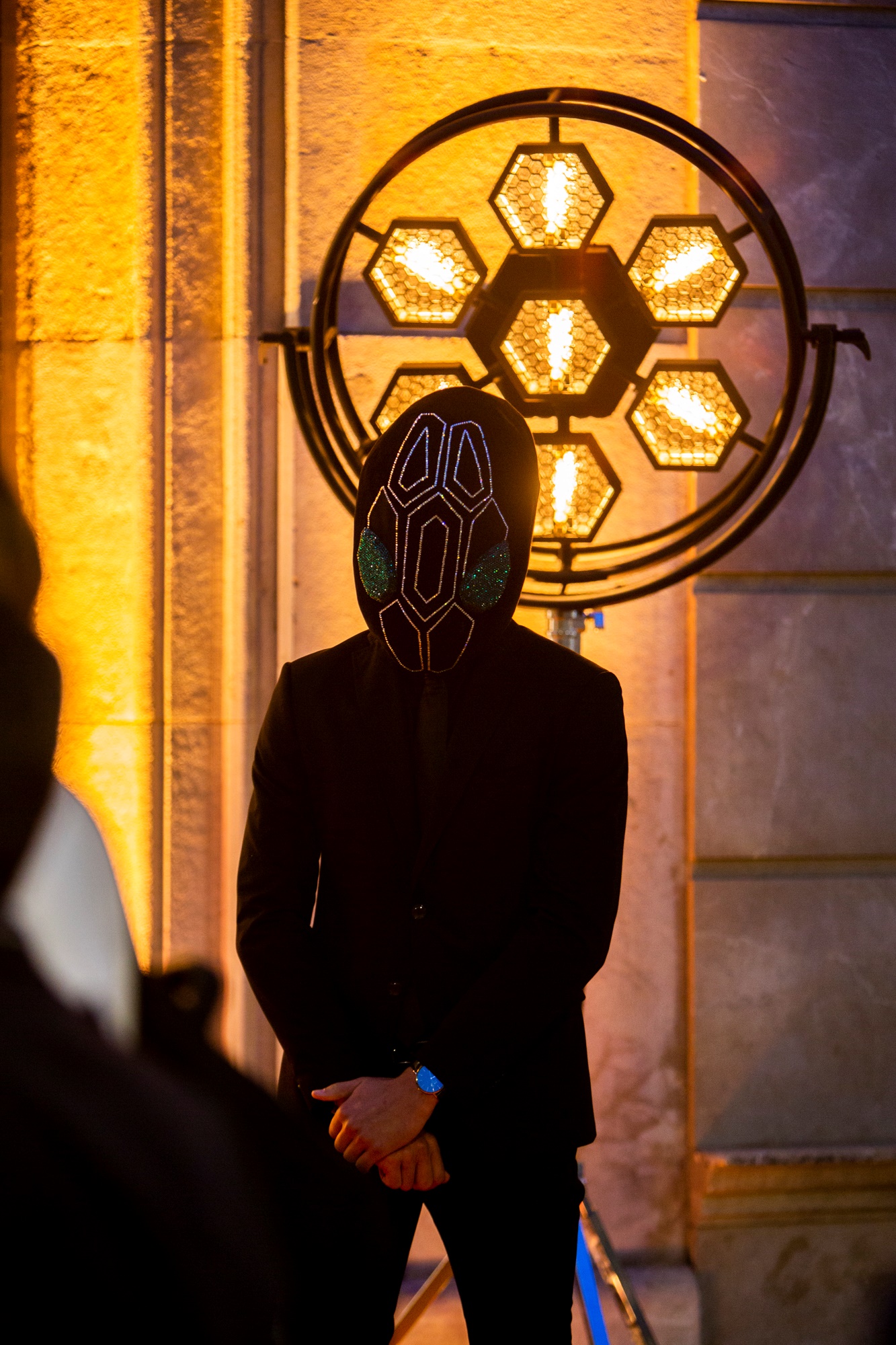 Invitado con máscara negra de patrón serpiente ante un panel luminoso hexagonal en la fachada, inauguración de la boutique Bvlgari Serpenti de Barcelona producida por ESMA Events