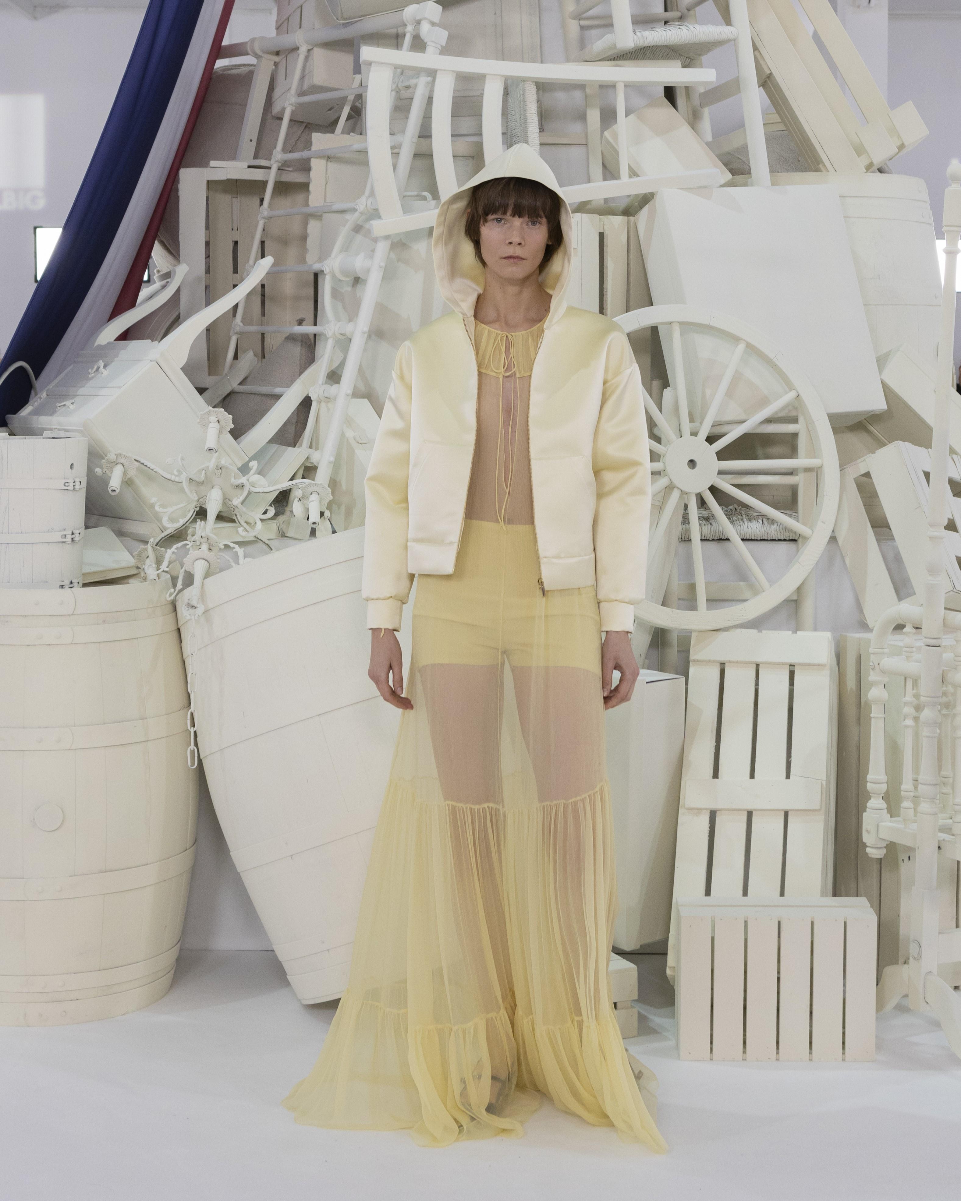 Model in a short yellow jacket and a long sheer yellow skirt in front of the installation, 1832 Sur Mer Teresa Helbig FW24/25 presentation produced by ESMA Events