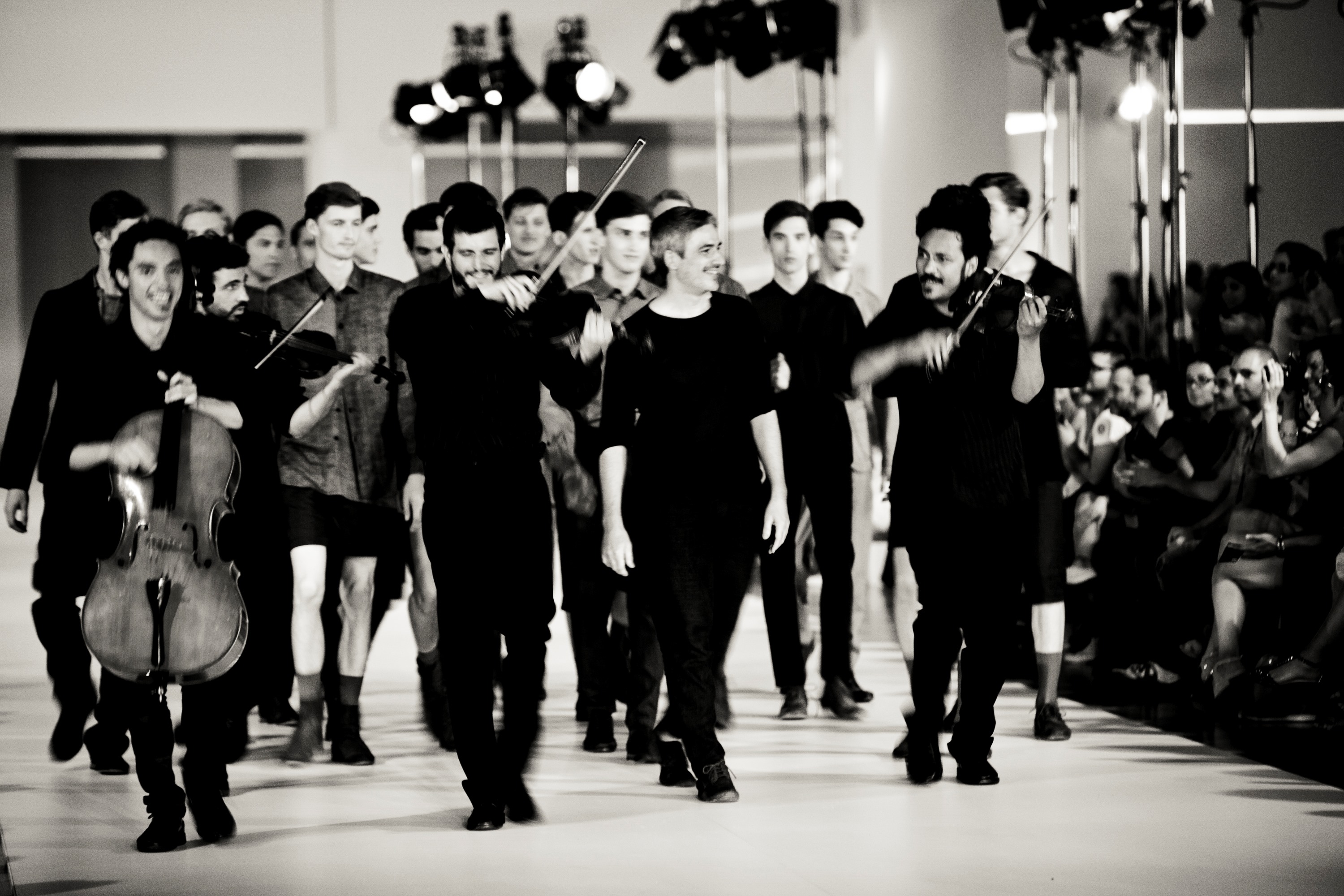 Modelos y músicos con violines y un violonchelo vestidos de negro en el final del desfile, en blanco y negro, 080 Barcelona Fashion SS 2014 producida por ESMA Events