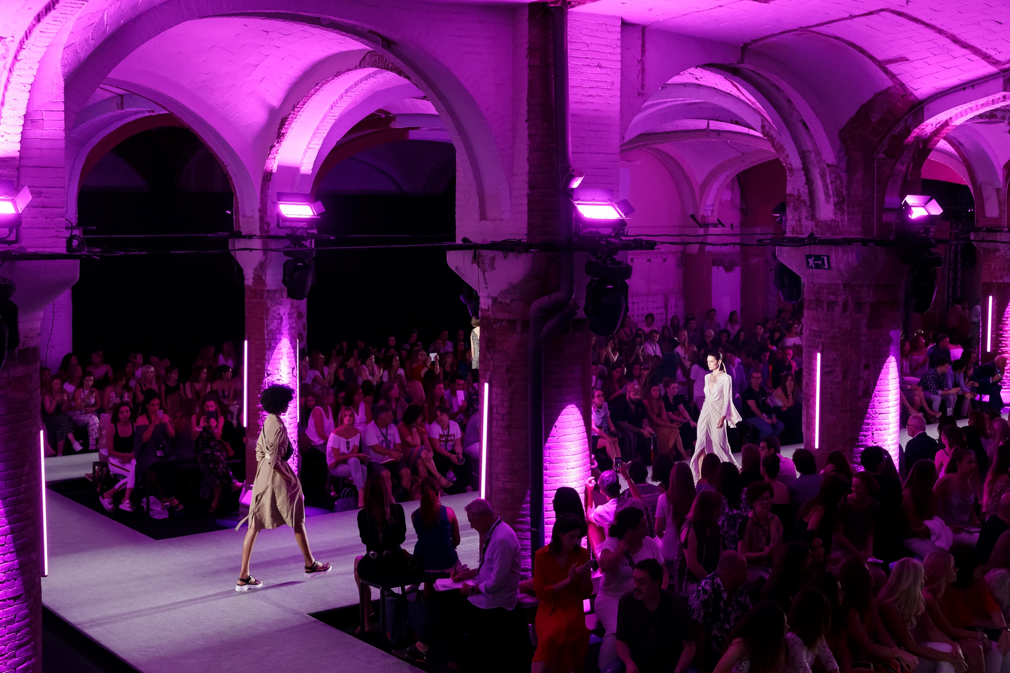 Sala de bóvedas de ladrillo iluminada en violeta con público a ambos lados de la pasarela, 080 Barcelona Fashion SS 2019 producida por ESMA Events