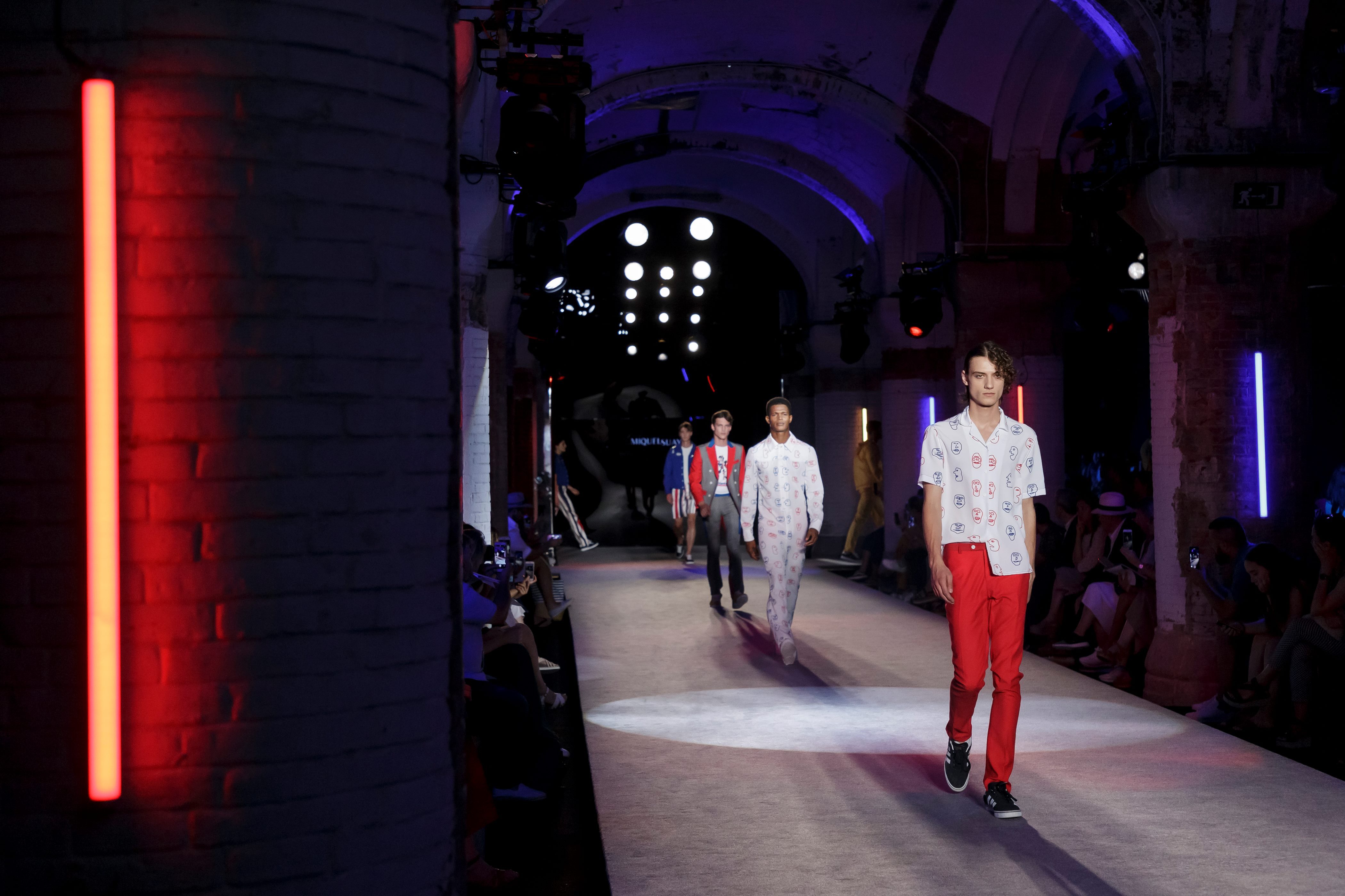 Modelos masculinos con pantalón rojo y camisas estampadas desfilando bajo bóvedas con luz azul, 080 Barcelona Fashion SS 2019 producida por ESMA Events