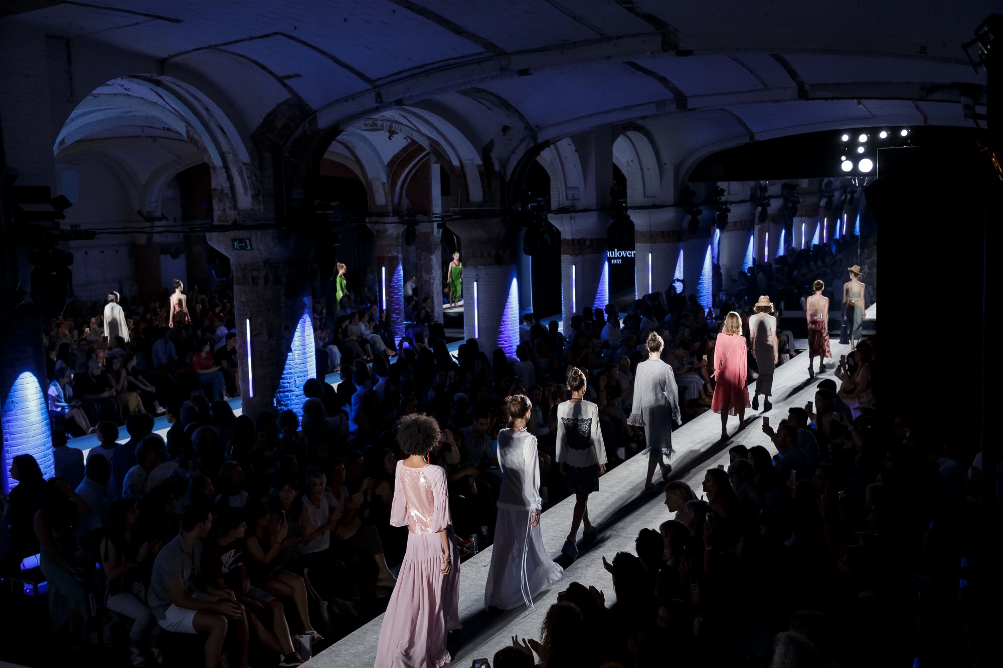 Vista general de la pasarela con modelos con vestidos rosas y claros entre el público bajo bóvedas, 080 Barcelona Fashion SS 2019 producida por ESMA Events