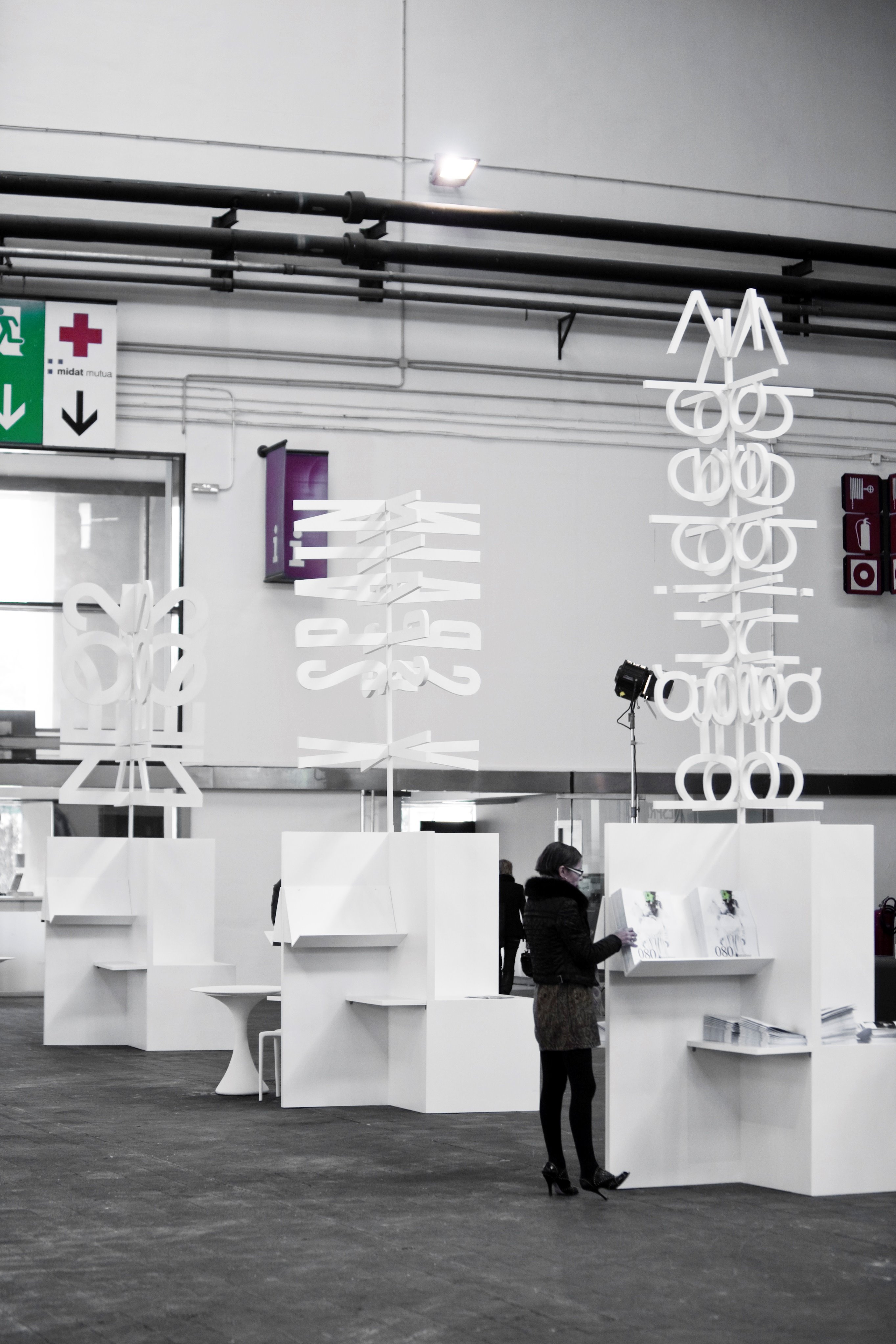 Showroom con mesas blancas y letras luminosas verticales, en blanco y negro, 080 Barcelona Fashion FW 2010-2011 producida por ESMA Events