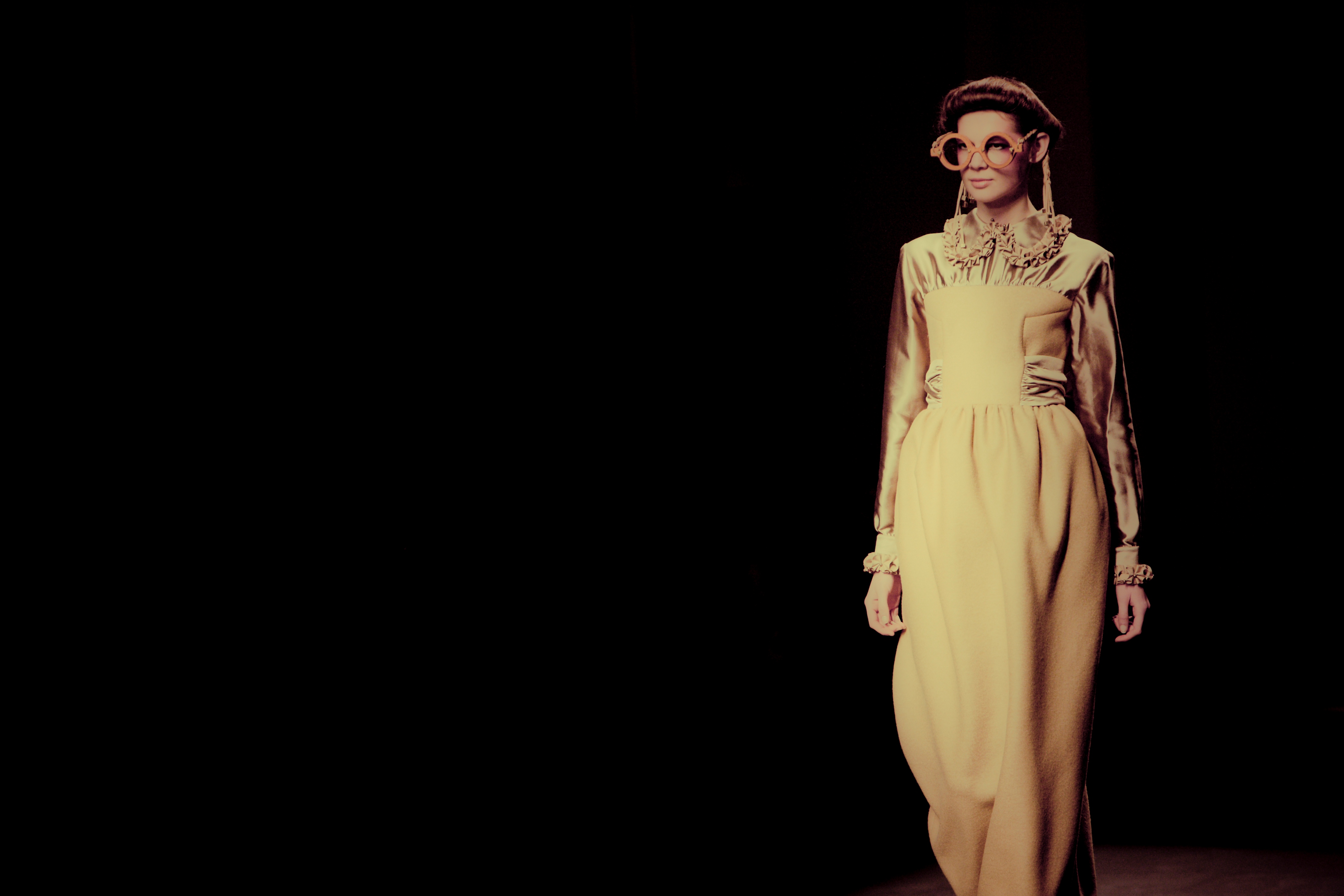 Modelo con gafas redondas y vestido largo amarillo sobre fondo negro, 080 Barcelona Fashion FW 2010-2011 producida por ESMA Events
