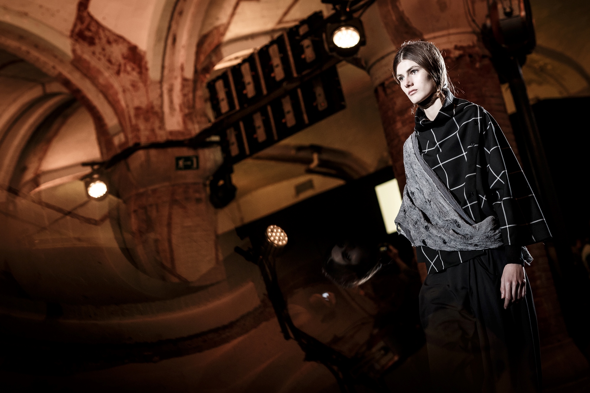 Modelo con jersey de cuadros ante una bóveda de ladrillo y un rótulo suspendido, 080 Barcelona Fashion FW 2018-2019 producida por ESMA Events