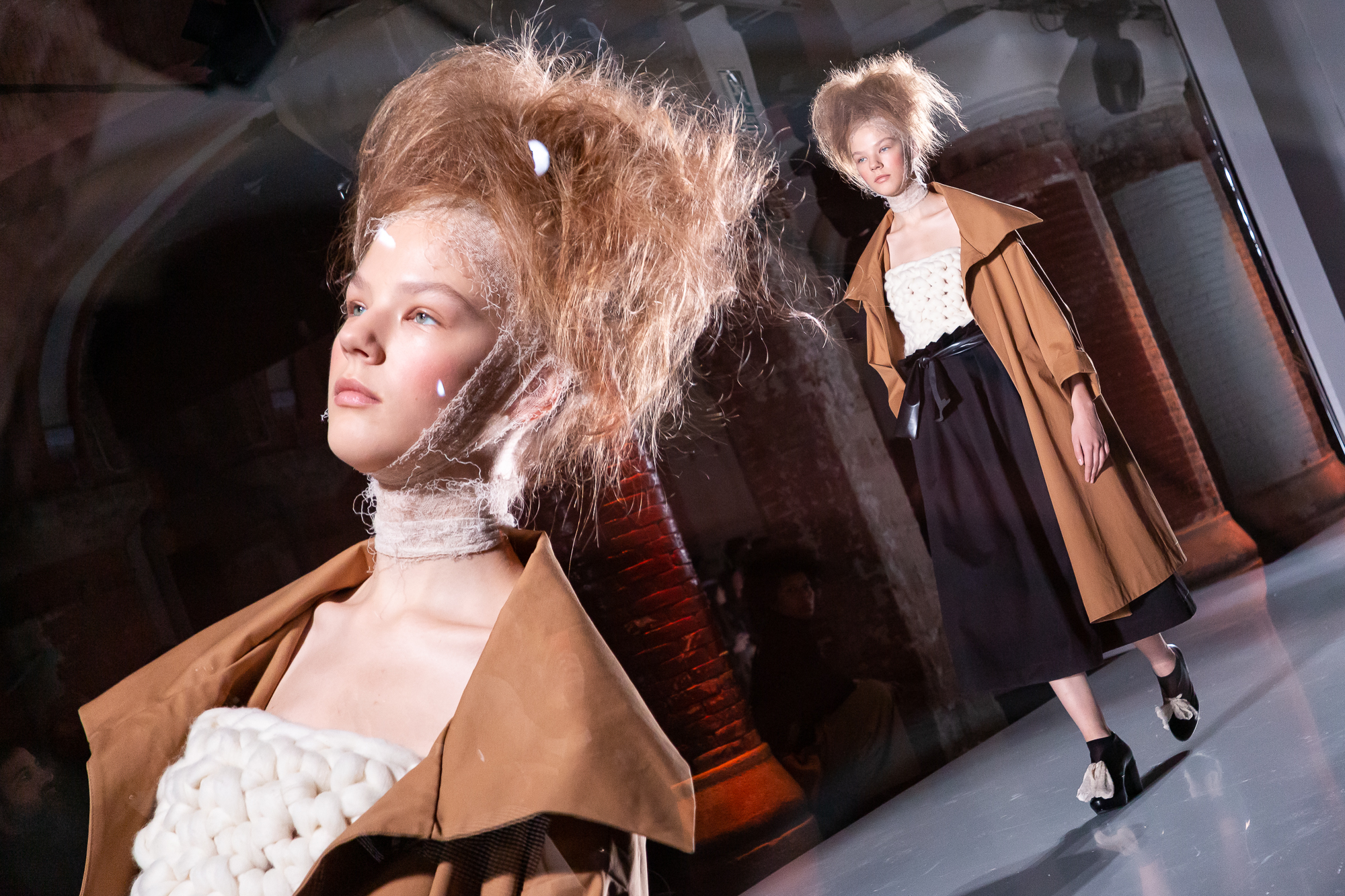 Modelo con peinado voluminoso y abrigo marrón sobre la pasarela, con otra modelo al fondo, 080 Barcelona Fashion FW 2019-2020 producida por ESMA Events