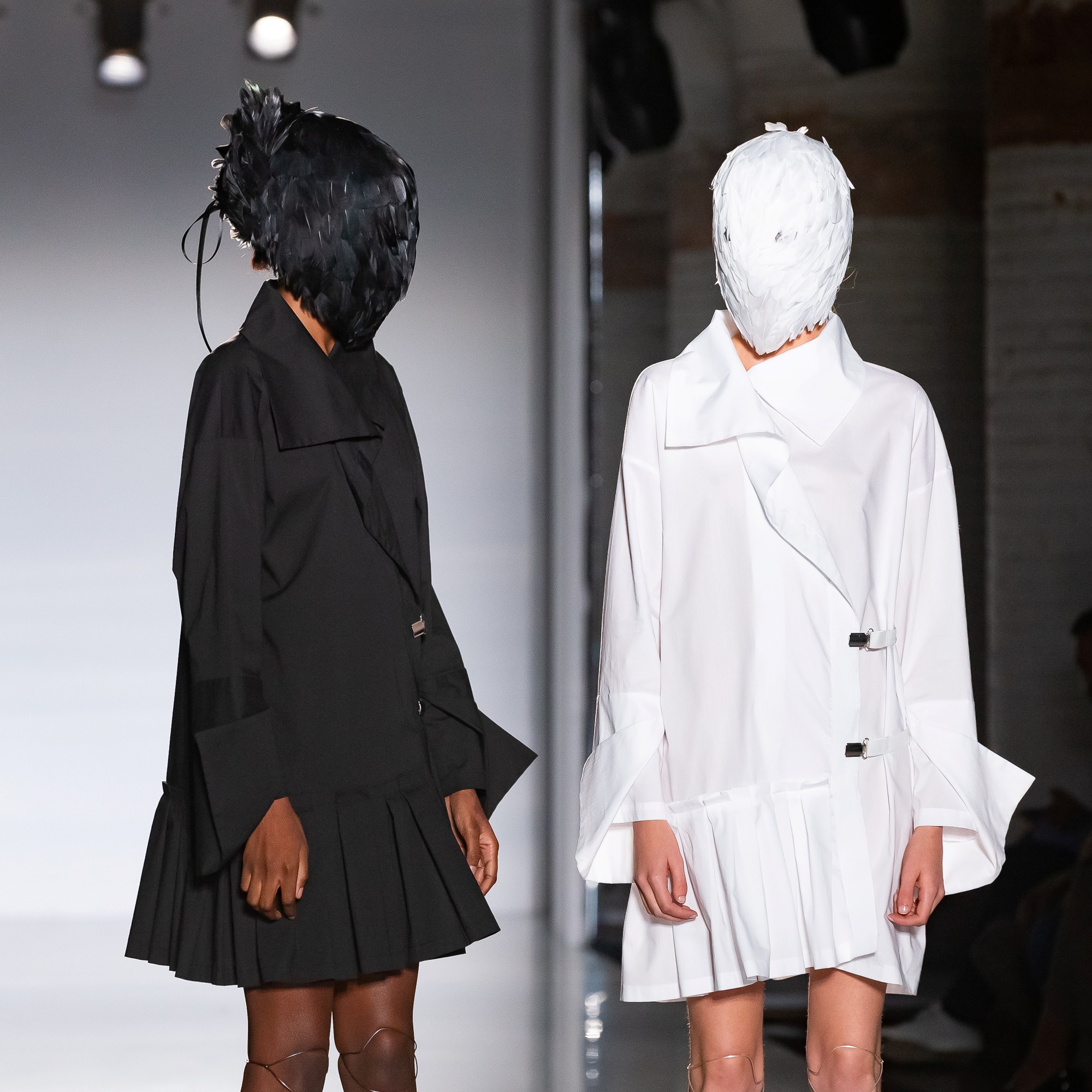 Dos modelos con la cabeza cubierta, una con vestido negro plisado y otra con vestido blanco, 080 Barcelona Fashion FW 2019-2020 producida por ESMA Events