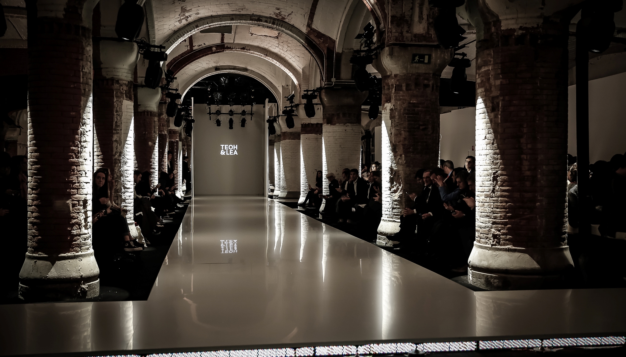 Pasarela blanca brillante entre columnas de ladrillo con el público a ambos lados, 080 Barcelona Fashion FW 2019-2020 producida por ESMA Events