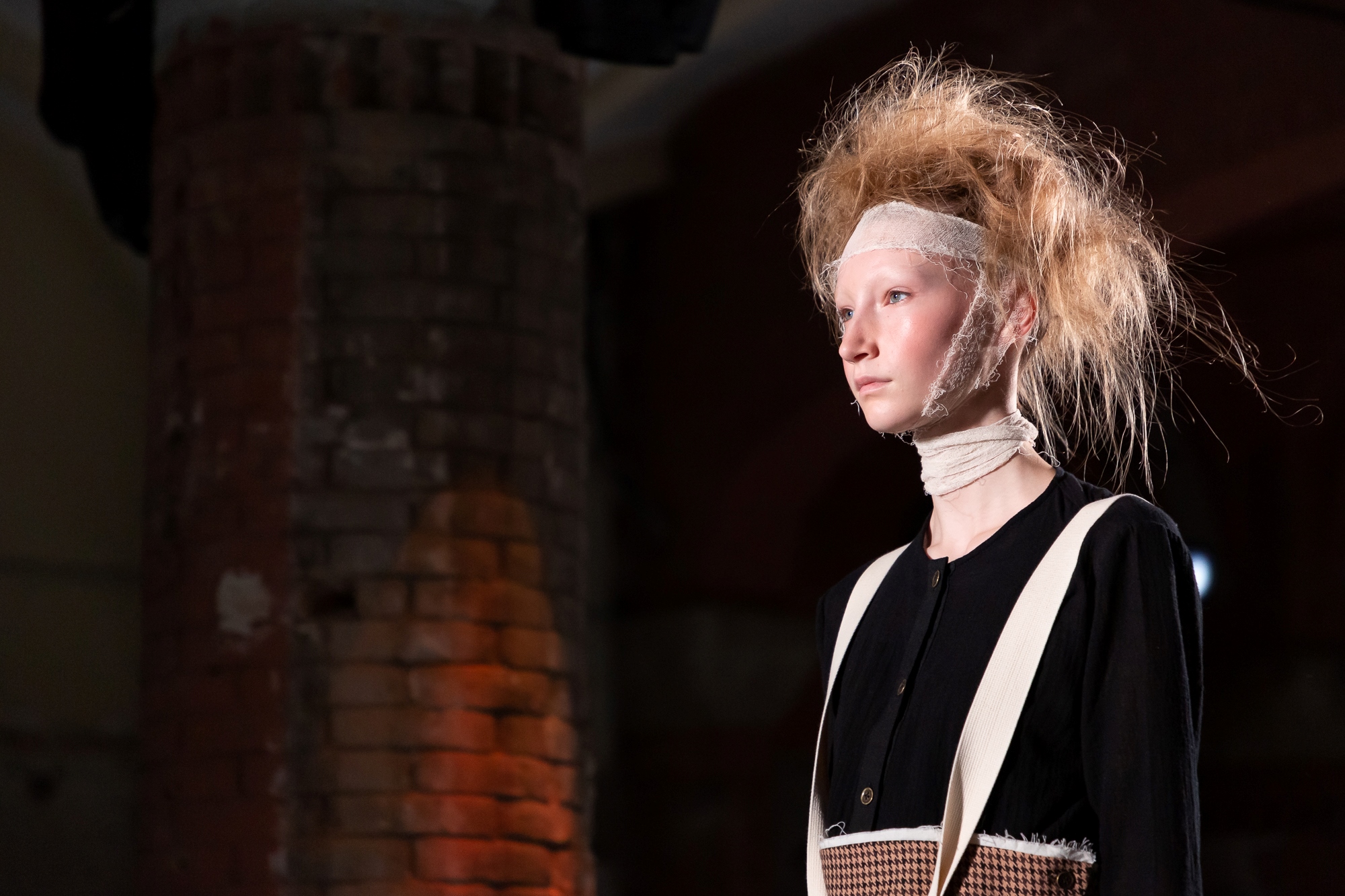 Retrato de una modelo con el pelo voluminoso y una venda en la frente ante una columna de ladrillo, 080 Barcelona Fashion FW 2019-2020 producida por ESMA Events