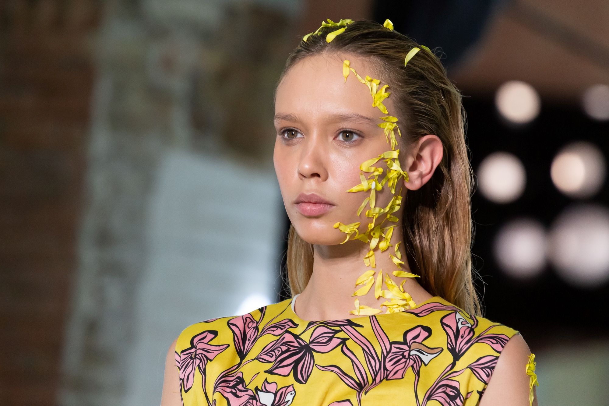 Retrato de una modelo con pétalos amarillos en la cara y vestido amarillo con flores rosas, 080 Barcelona Fashion FW 2019-2020 producida por ESMA Events