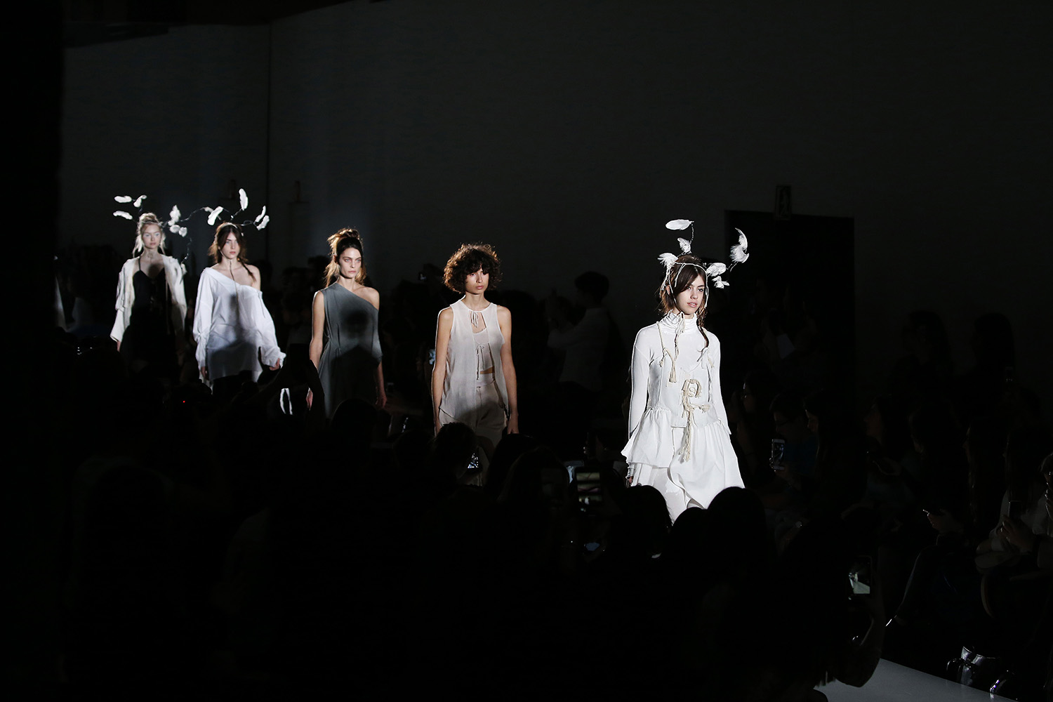 Modelos con tocados de plumas blancas al fondo de una sala oscura, 080 Barcelona Fashion FW 2019-2020 producida por ESMA Events