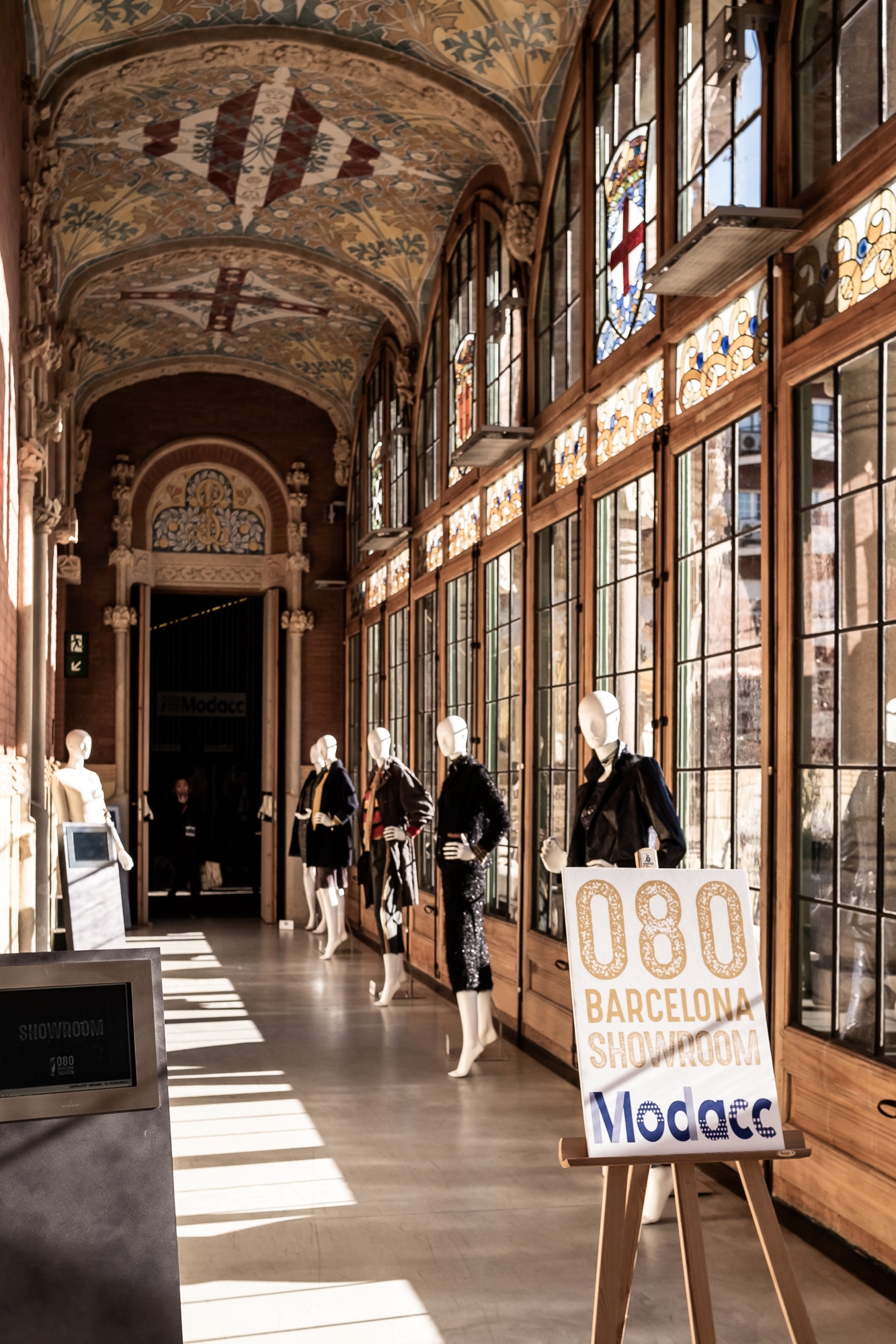 Pasillo del recinto con maniquíes expuestos y un caballete con el cartel del 080 Barcelona Fashion, 080 Barcelona Fashion FW 2019-2020 producida por ESMA Events