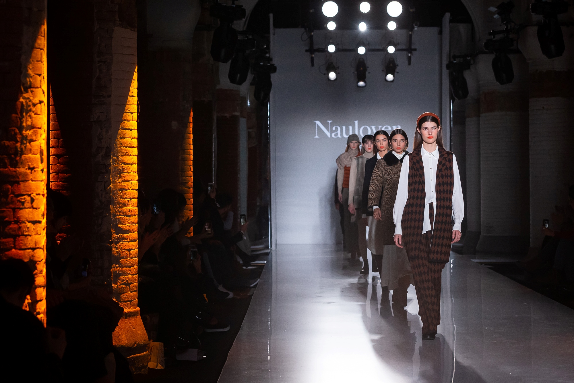 Modelos desfilando con prendas de cuadros ante el rótulo Naulover entre columnas de ladrillo, 080 Barcelona Fashion FW 2019-2020 producida por ESMA Events