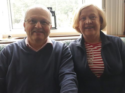 Alan and Avril, sitting together on a couch in their house. Happy after having taken our planning for retirement programme