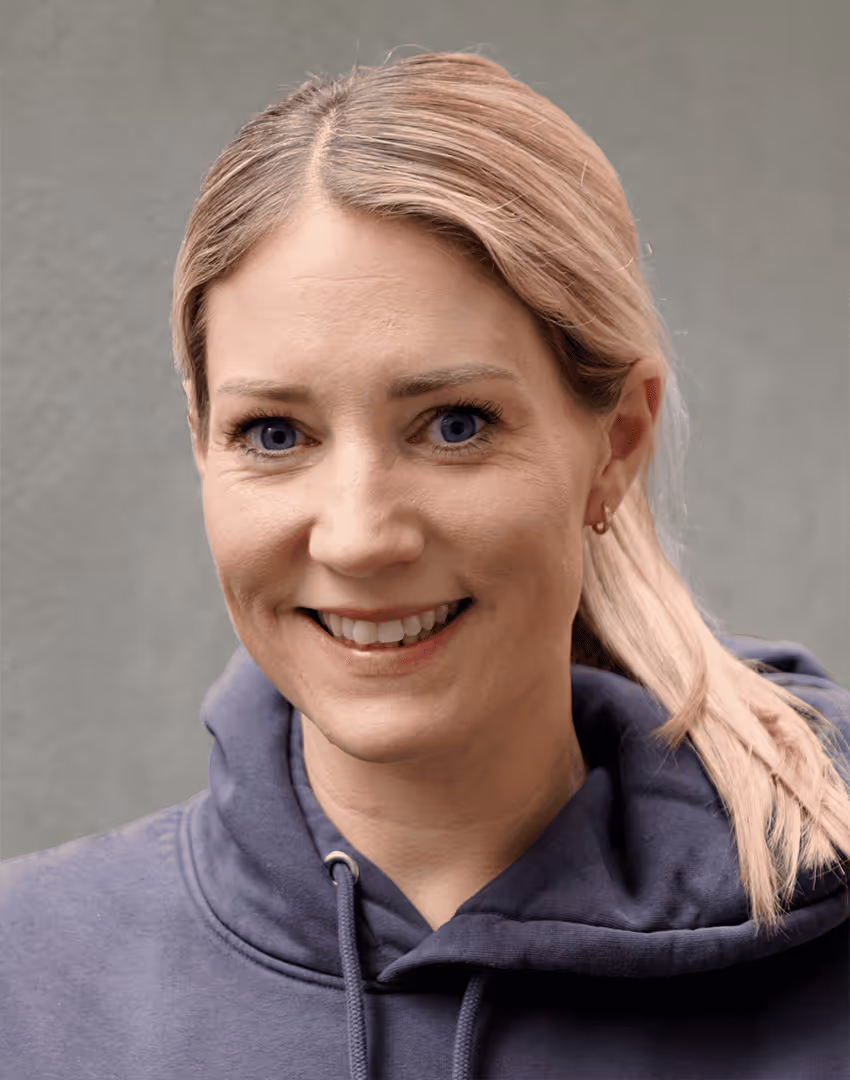 Porträt von Annika Appelhoff, kaayo-Team, in blauem Kapuzenpullover vor grauer Betonwand.
