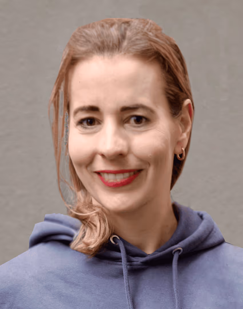 Lächelnde kaayo-Mitarbeiterin in blauem Kapuzenpullover vor grauer Betonwand.