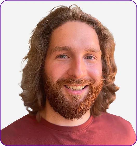 Smiling man with curly brown hair and a beard wearing a maroon shirt against a gray background.