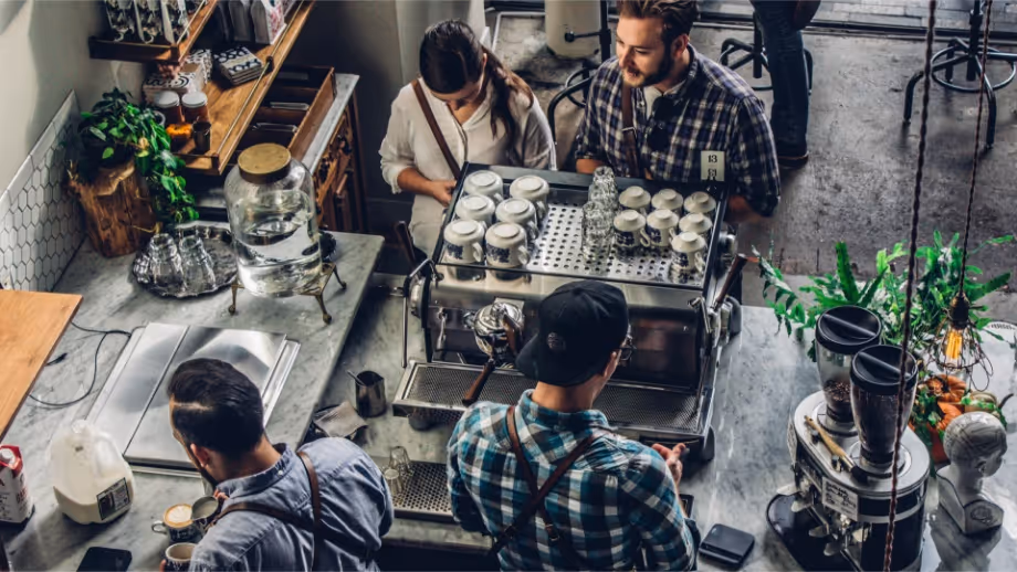 Workers at a neighborhood coffee shop serve two waiting customers.  