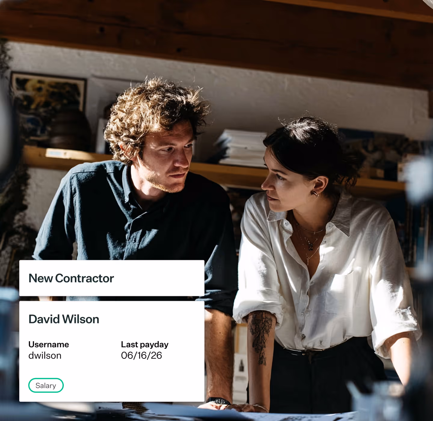 Two people leaning on a table discussing work with an overlay showing new contractor David Wilson details.
