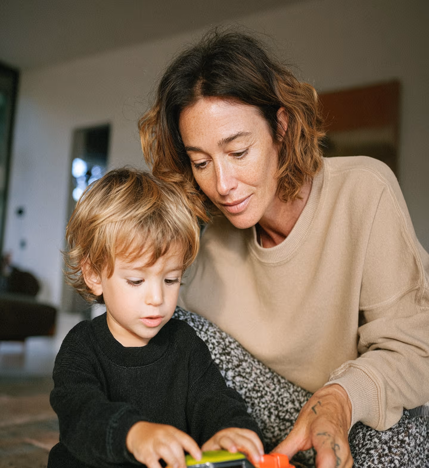 Woman and young boy play together indoors, focusing on a toy car in the boy's hands.