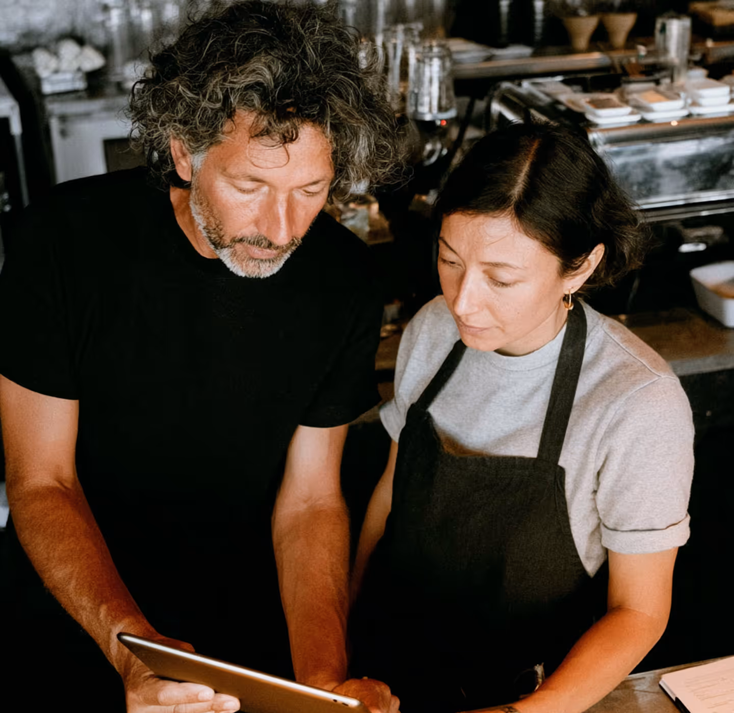 Two baristas looking intently at a tablet in a coffee shop.