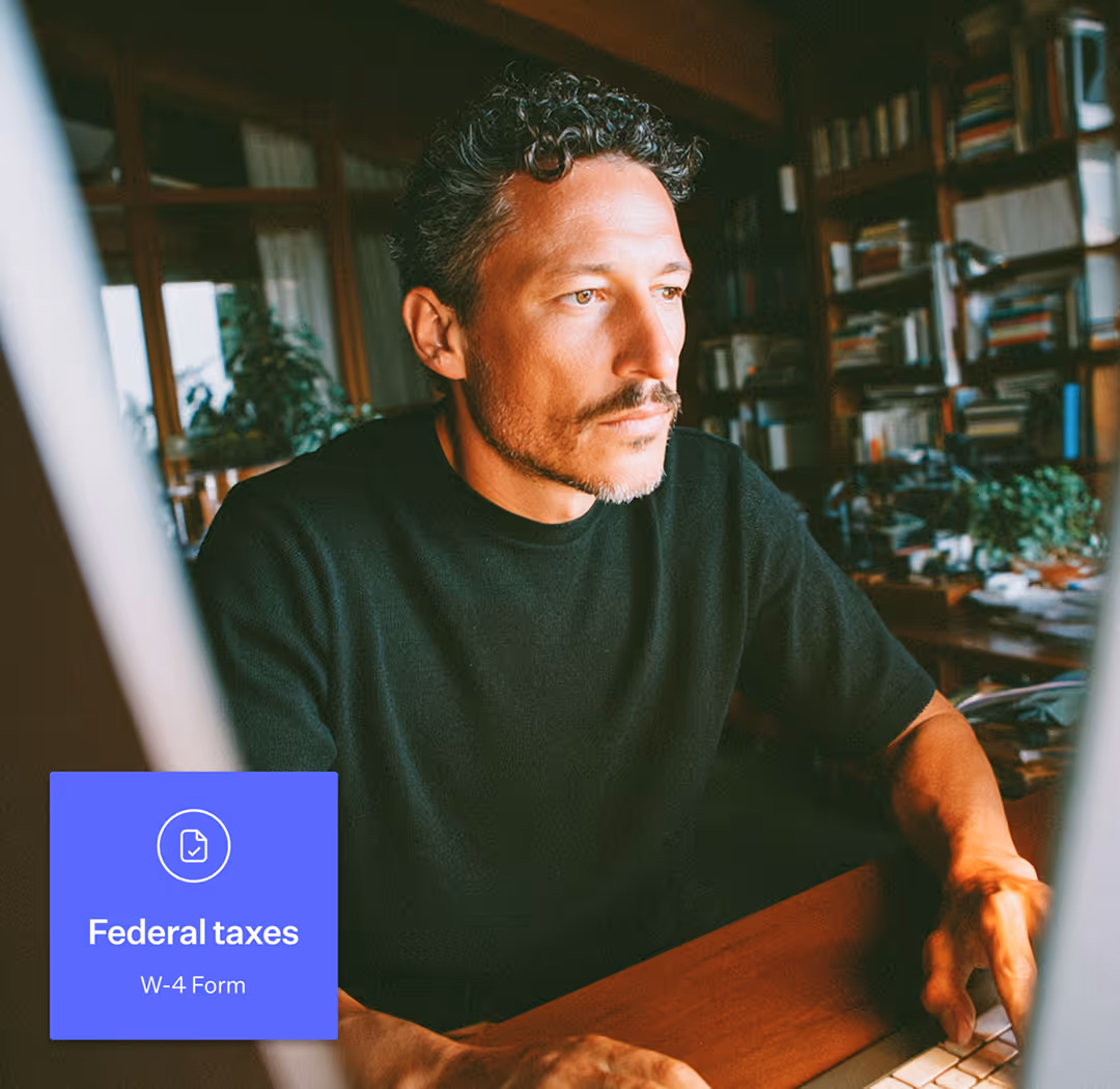 Man in black shirt focused on working at a computer in a room with bookshelves and plants.