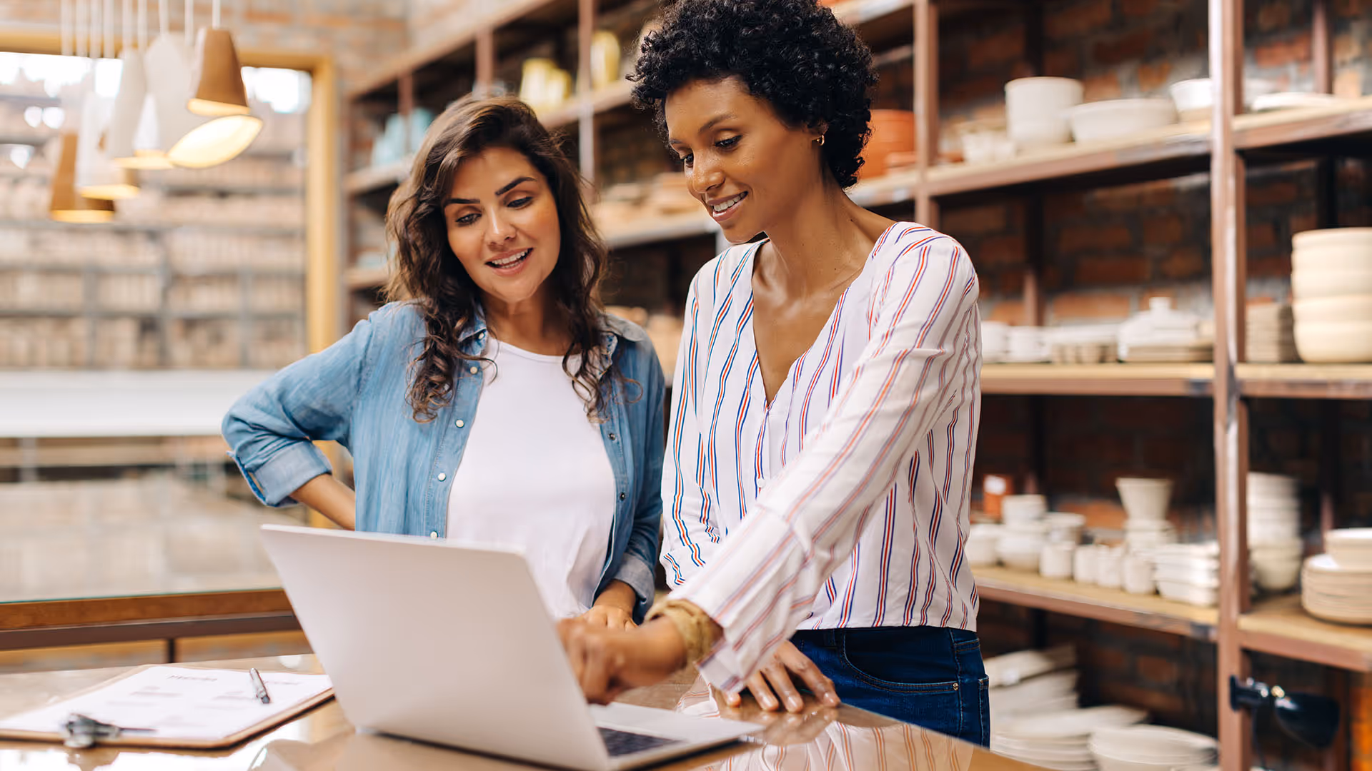 Two women using a laptop to run payroll for their pottery shop. 