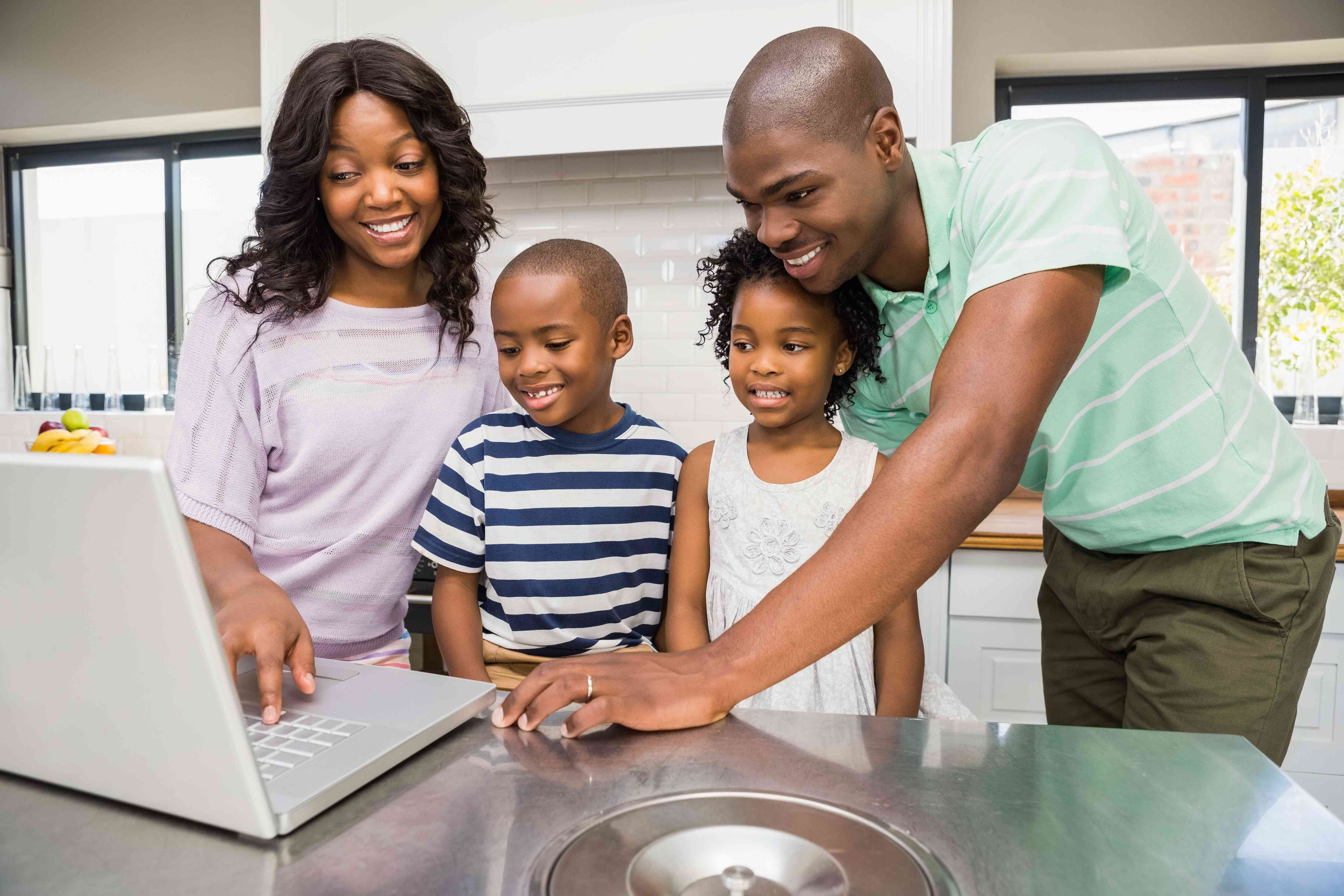 Happy family uses laptop to review nanny and household employer registration. 