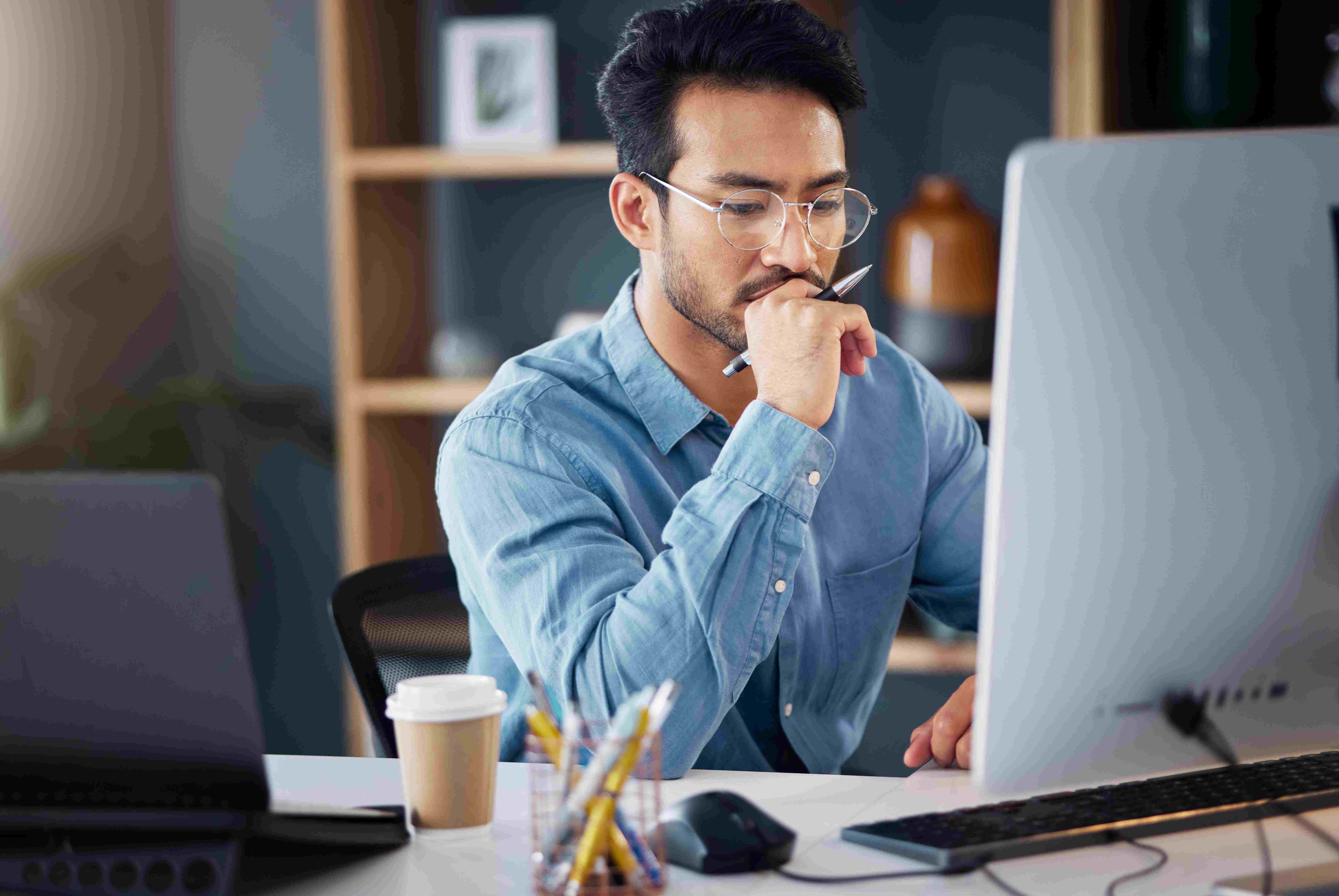 Lawyer sitting at desk, holding pen, looking at computer monitor, reviewing law firm payroll options.