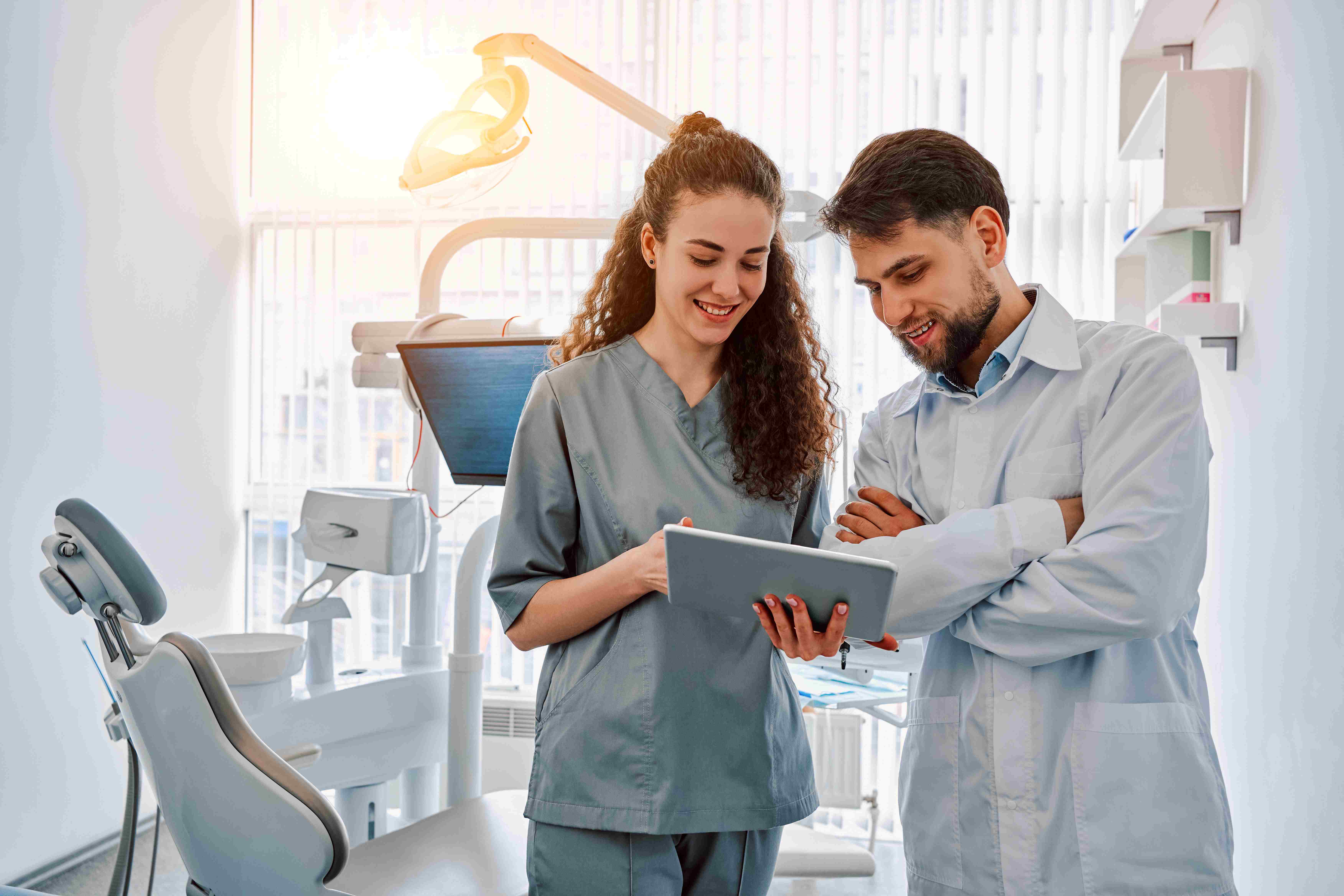 Two dentists standing in a dental office exam room reviewing information on a tablet.