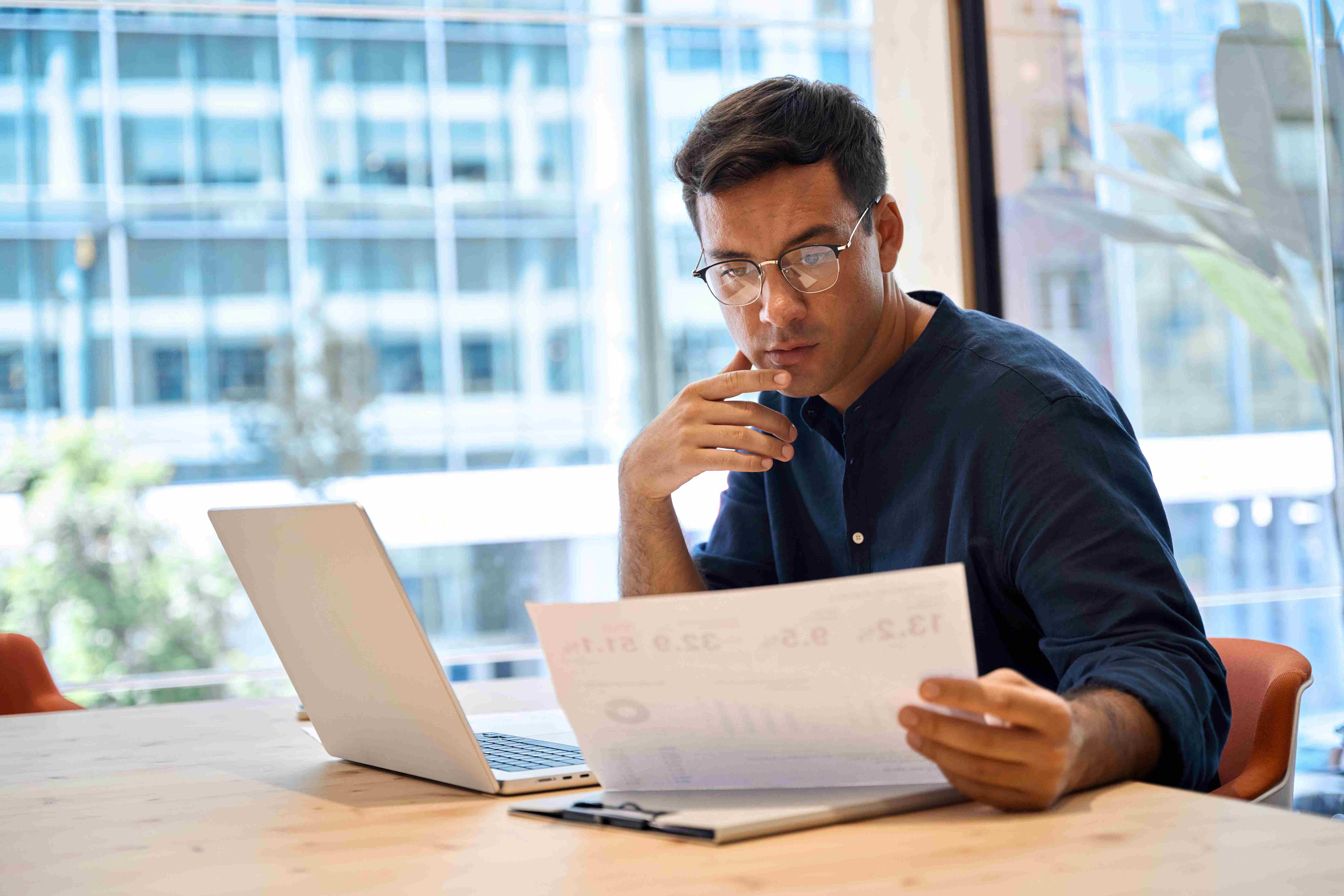 S-corp owner reviews financial data determine payroll at desk with paperwork and laptop.