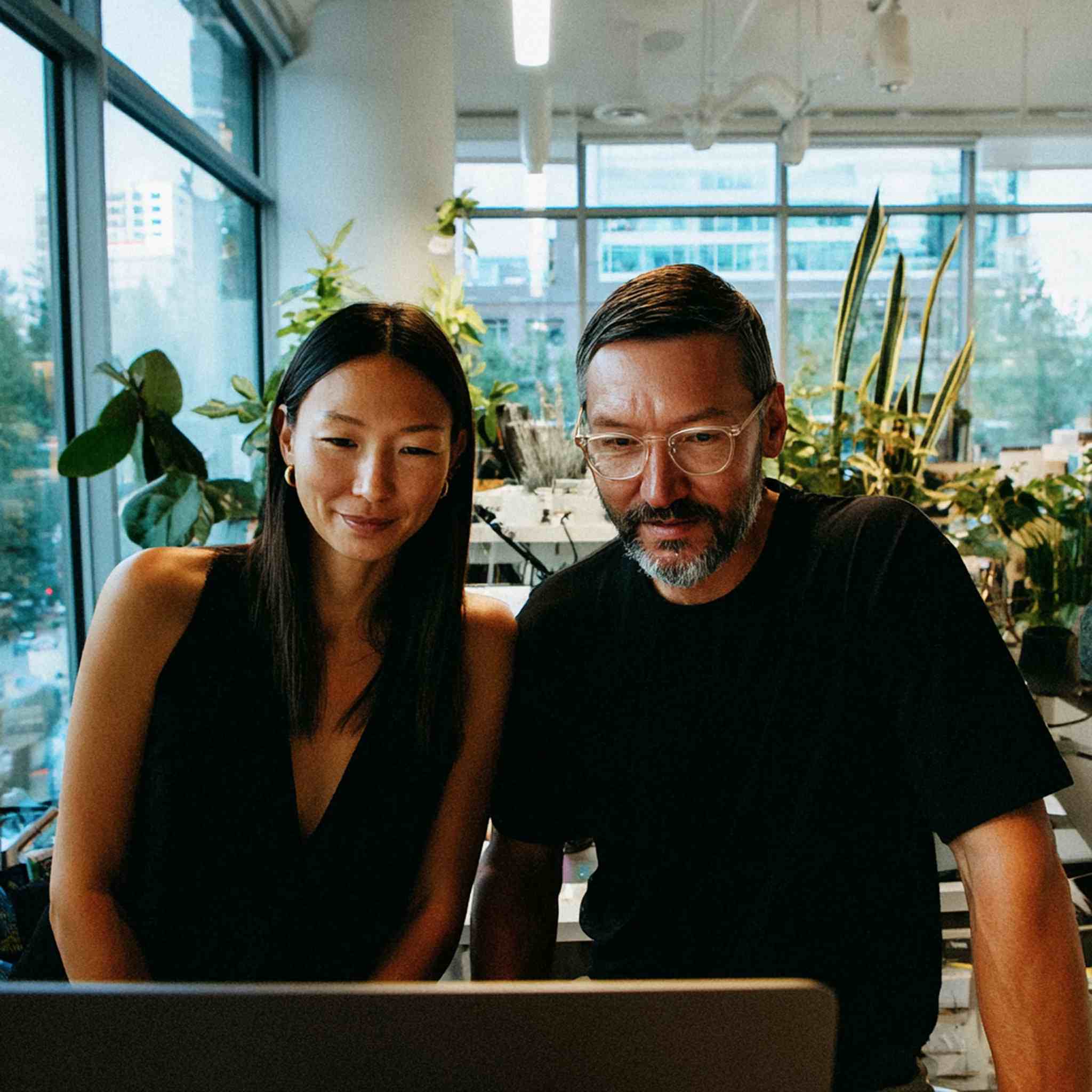 Two workers looking at computer on desk with plants behind them
