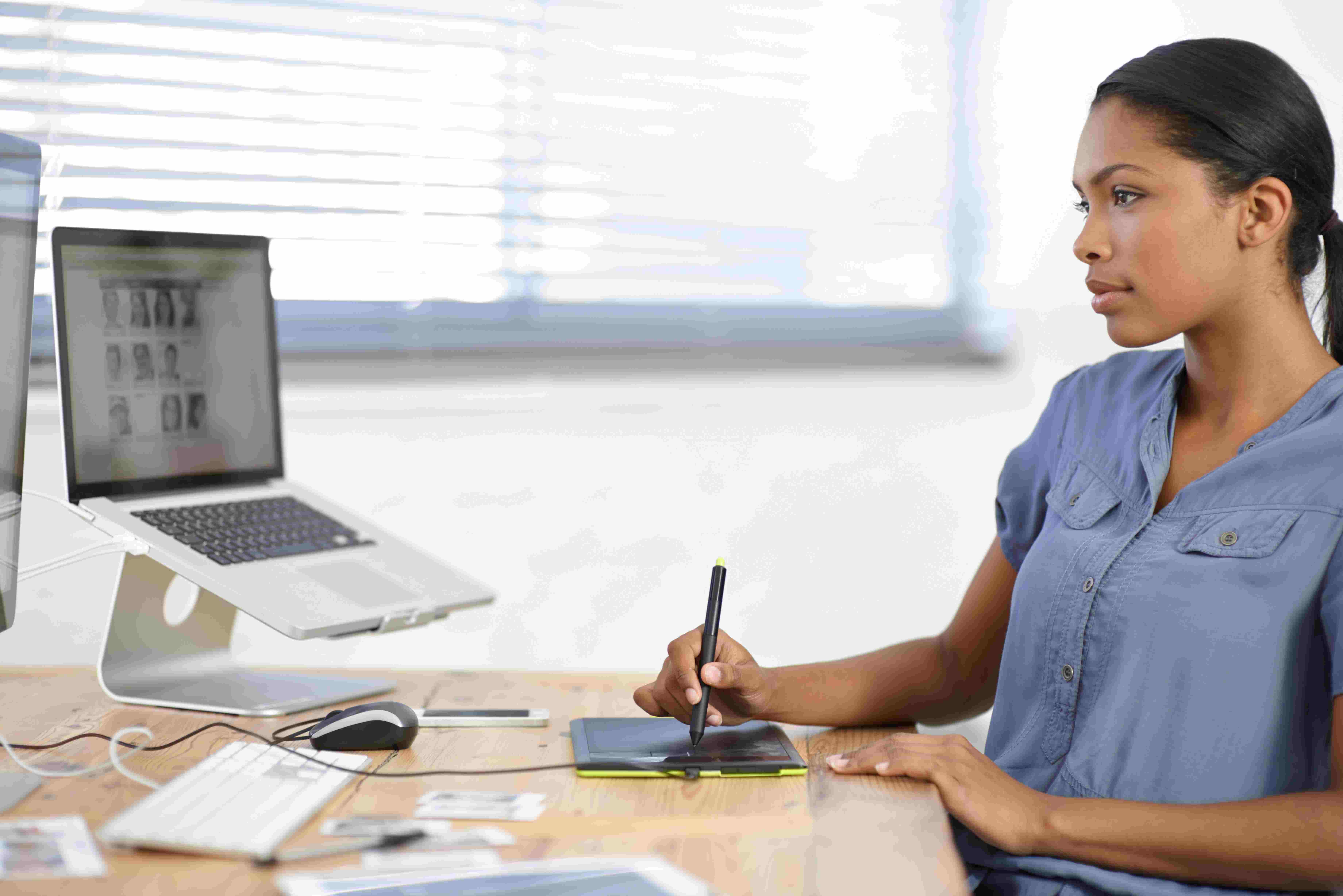 Sole proprietor graphic designer completes work for client on laptop at desk. 