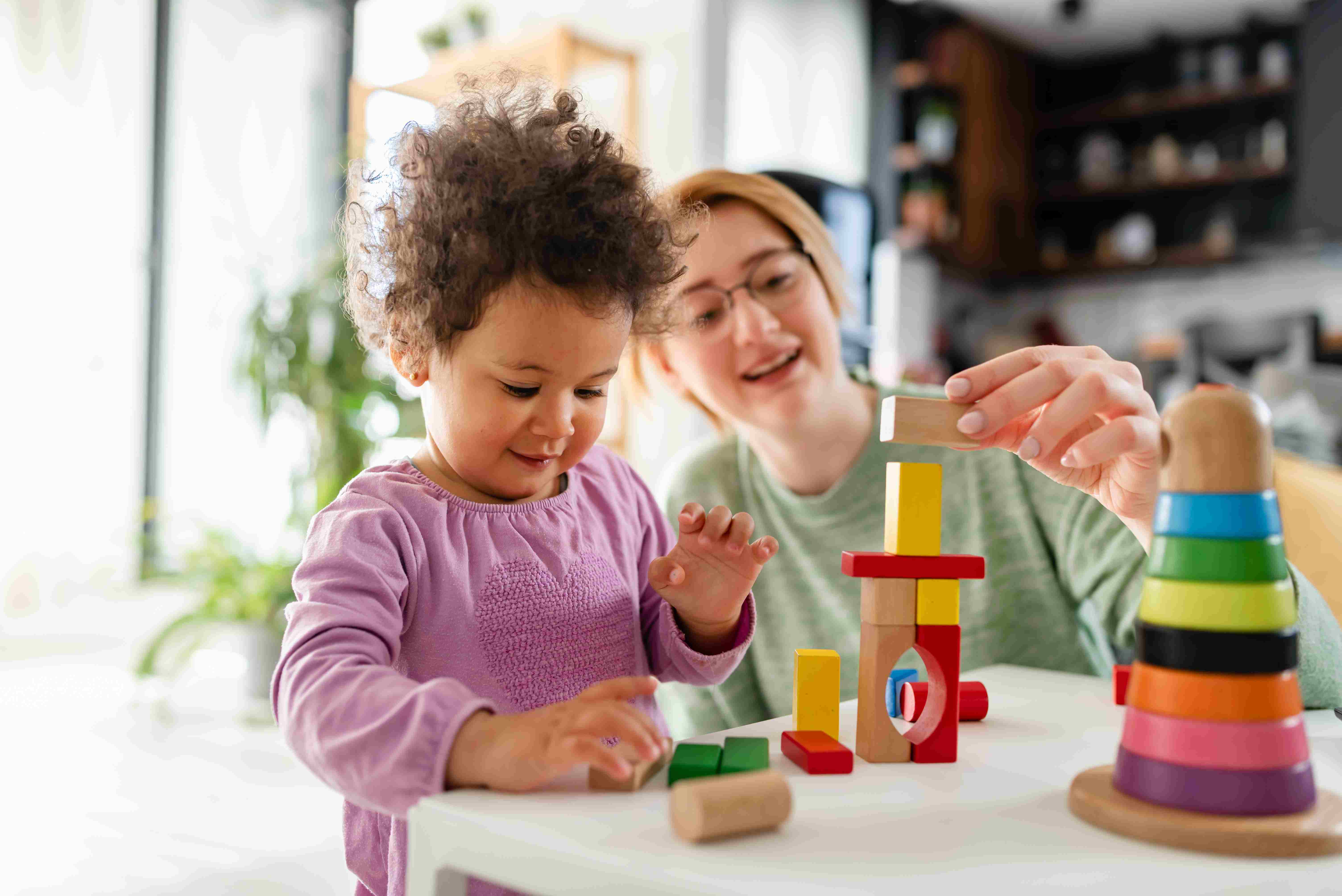 Nanny and child play with blocks at table in home.